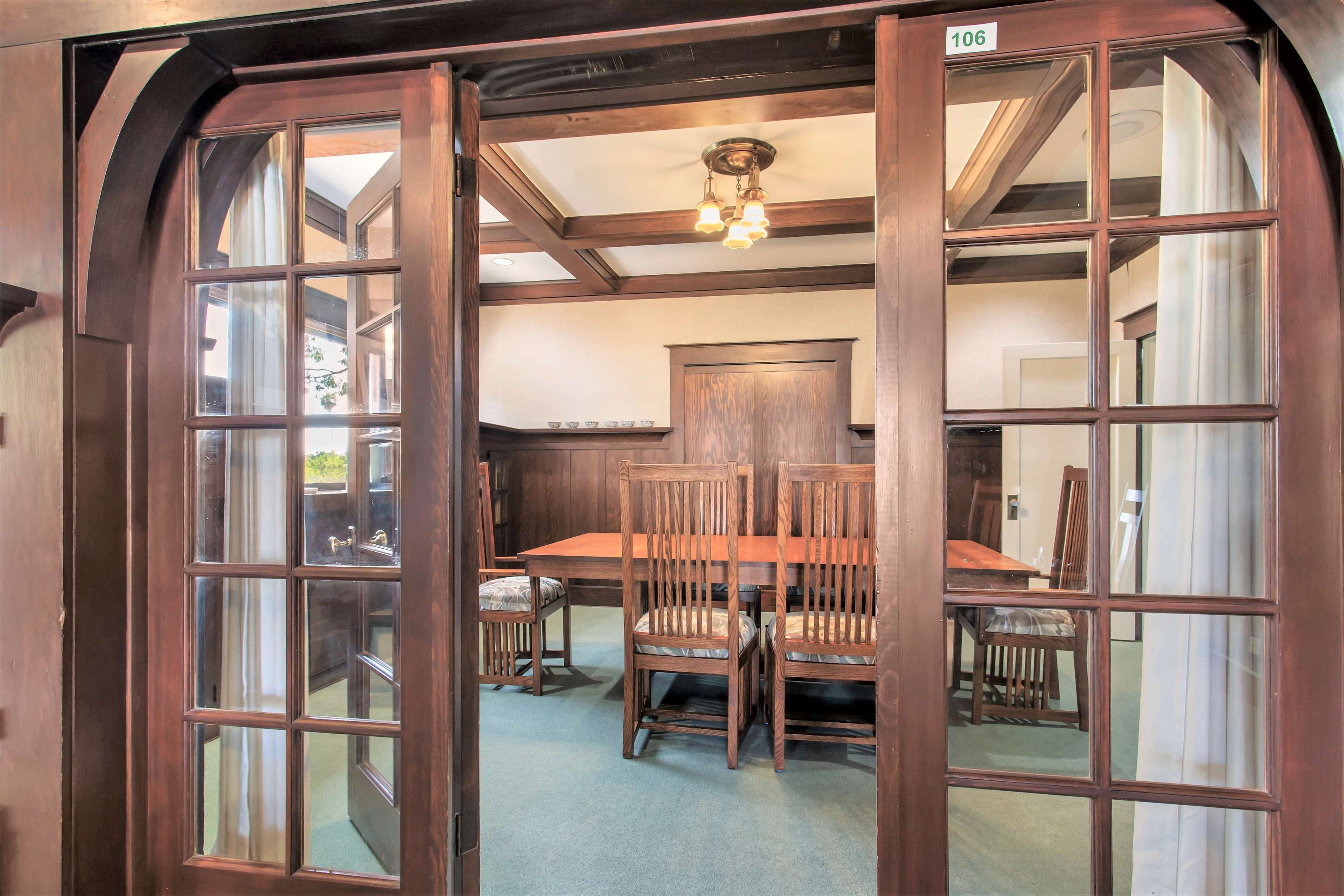 A room with a wooden table and six chairs is visible through double glass doors, showcasing a coffered ceiling and wall paneling.