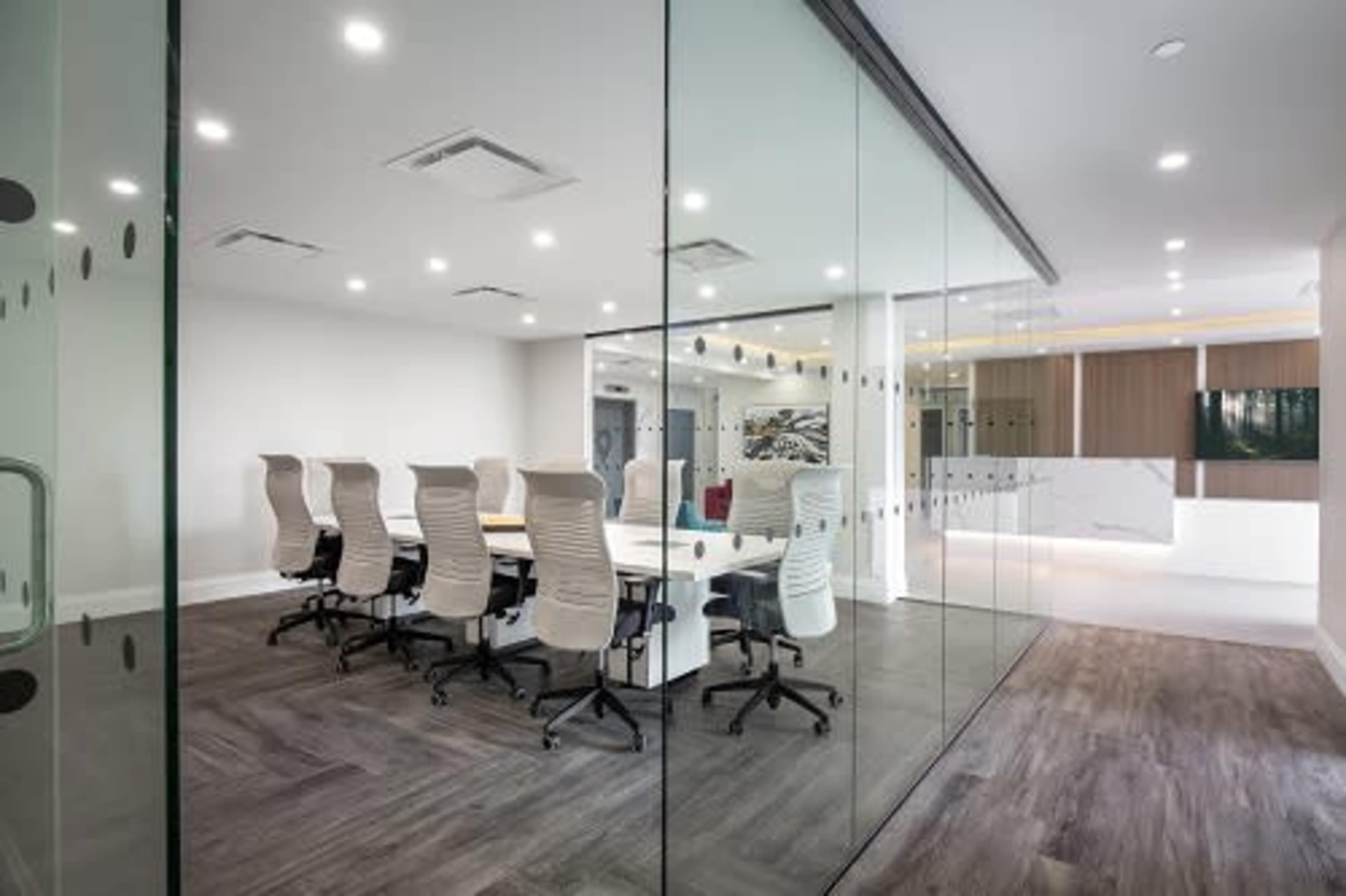 A modern conference room with a long table surrounded by ergonomic chairs, enclosed by glass walls.