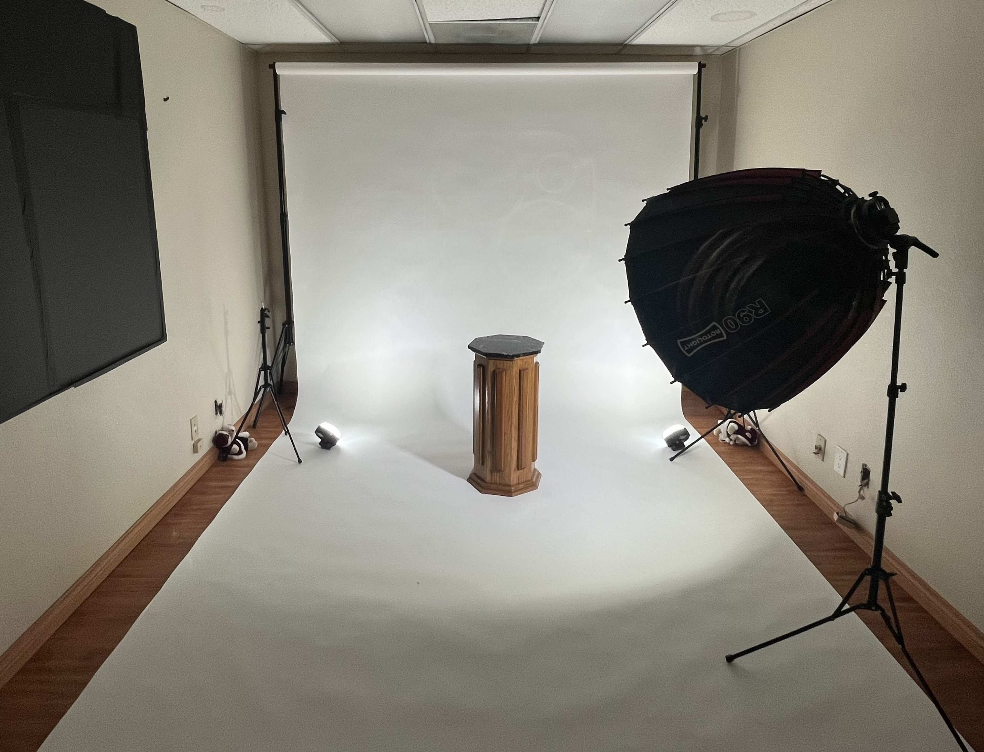 A photography studio setup featuring a wooden pedestal illuminated by studio lights against a white backdrop.