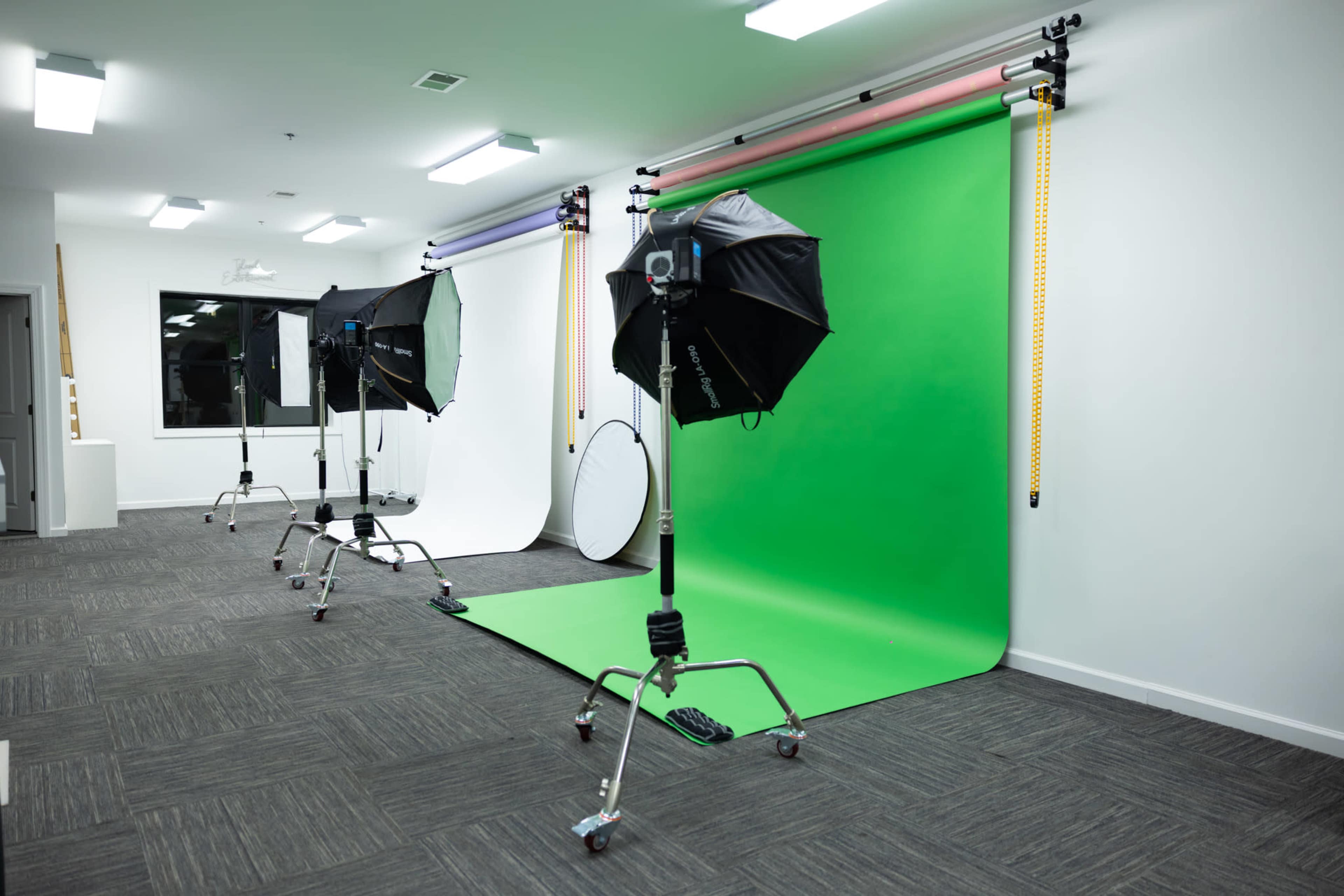 The image shows a photography studio with three backdrop options: green, white, and black, equipped with lighting setups on stands.