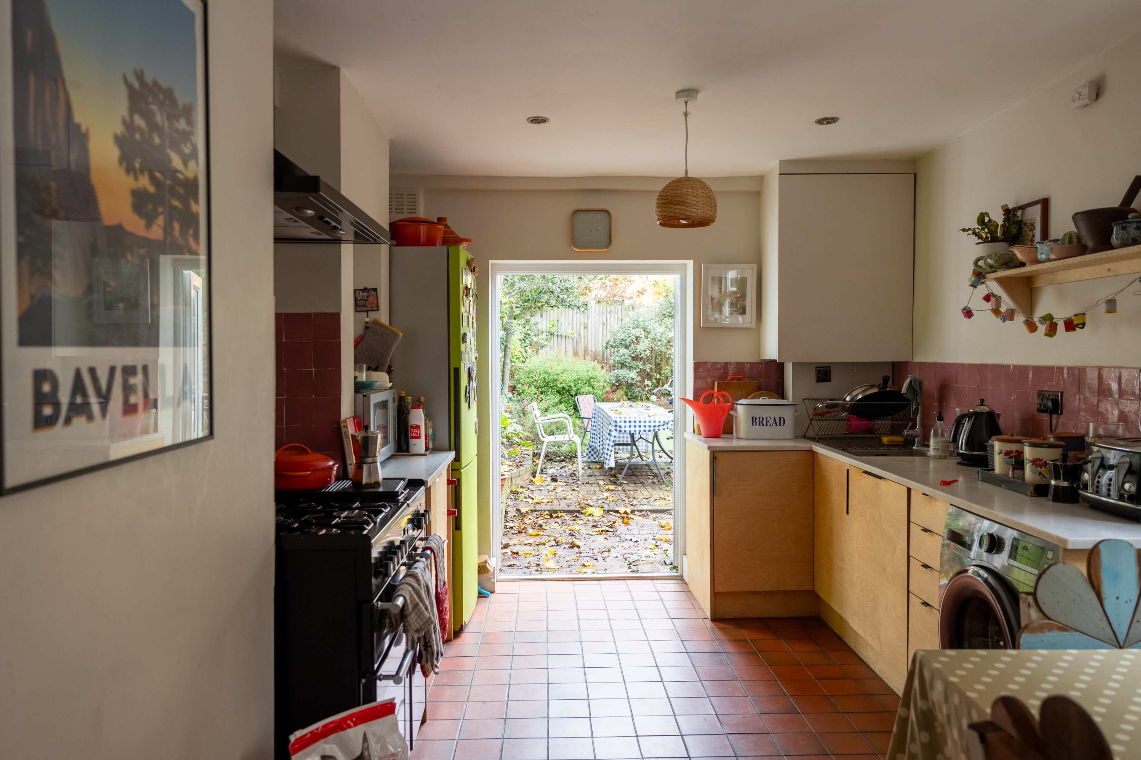 A bright kitchen with a view of a garden, featuring a gas stove, wooden cabinets, and a door leading outside.