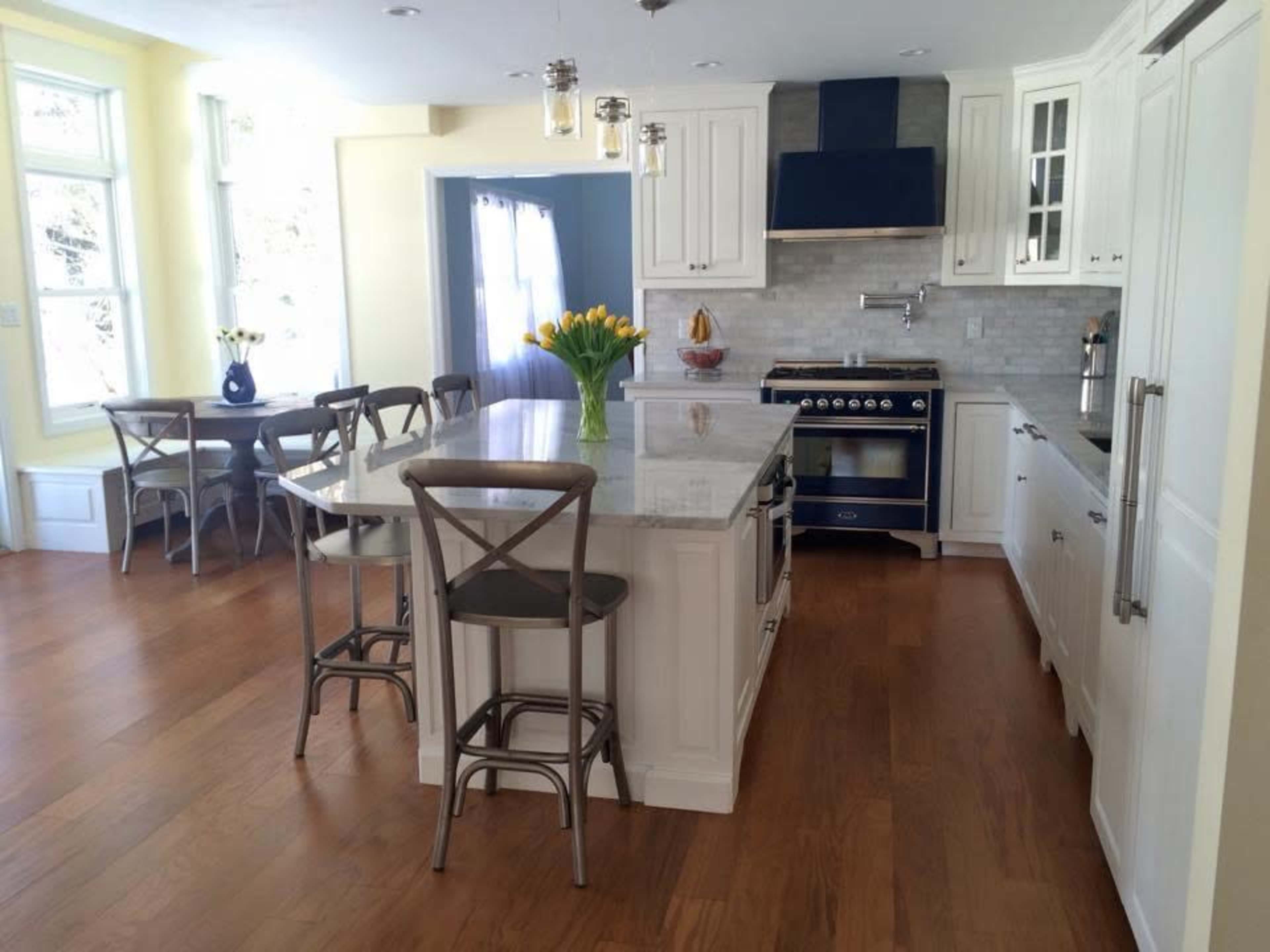 A modern kitchen with a central island, white cabinets, stainless steel appliances, and a dining area with a table and chairs.