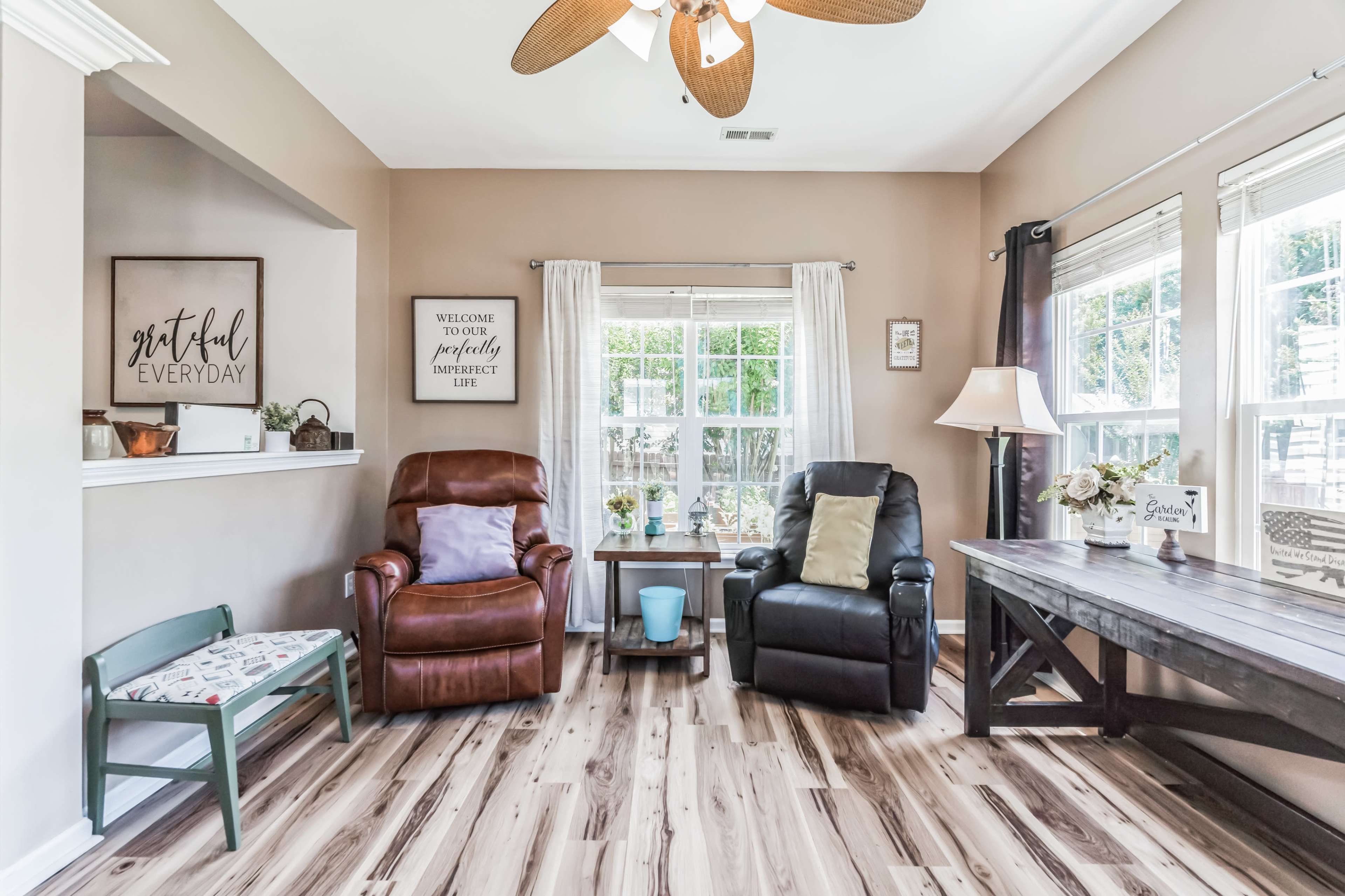 The living room features two armchairs, a coffee table, and large windows allowing natural light to enter.