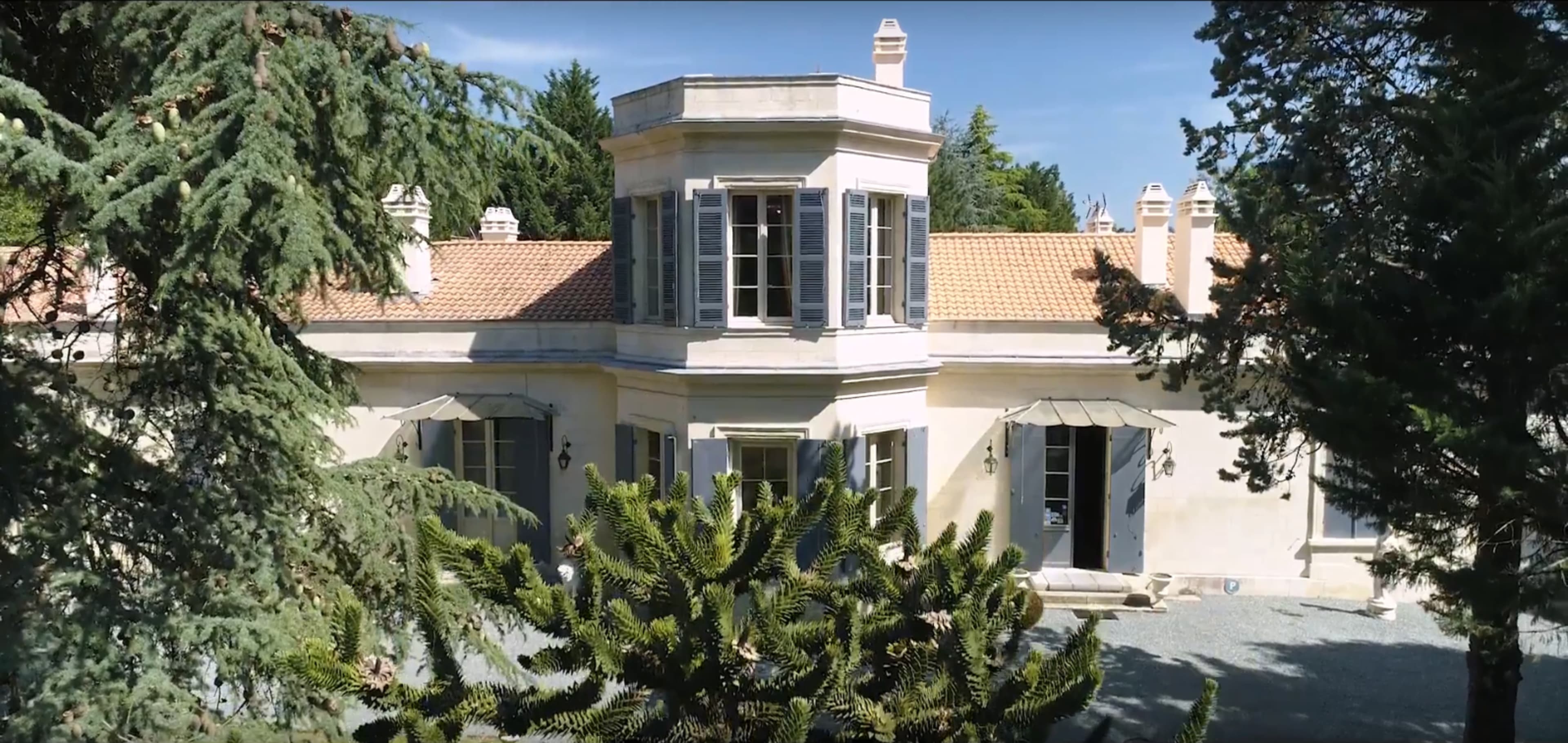 A large house with a central tower, surrounded by trees and a gravel path.