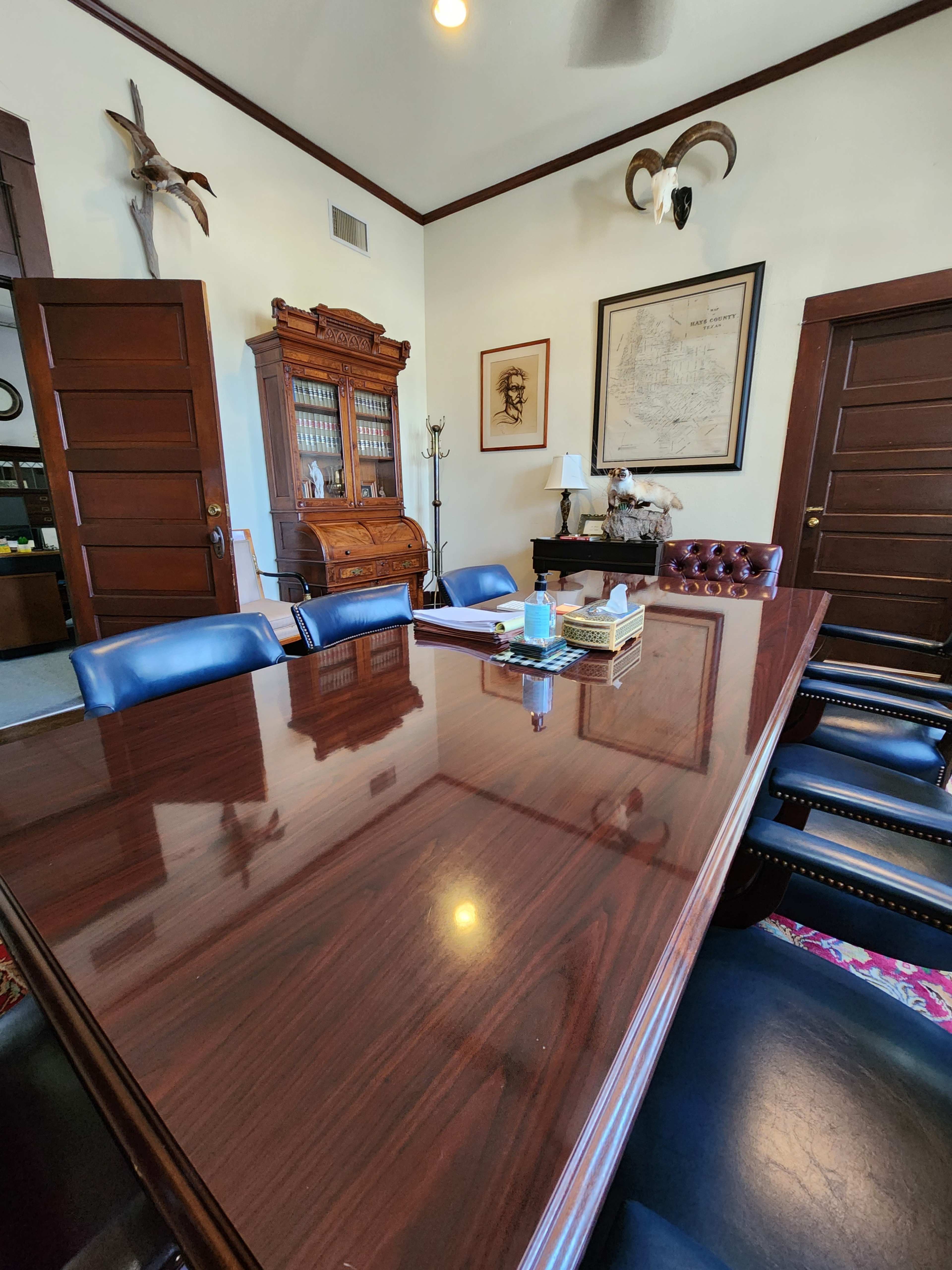 A formal conference room with a polished wooden table, leather chairs, and a large antique cabinet against the wall.
