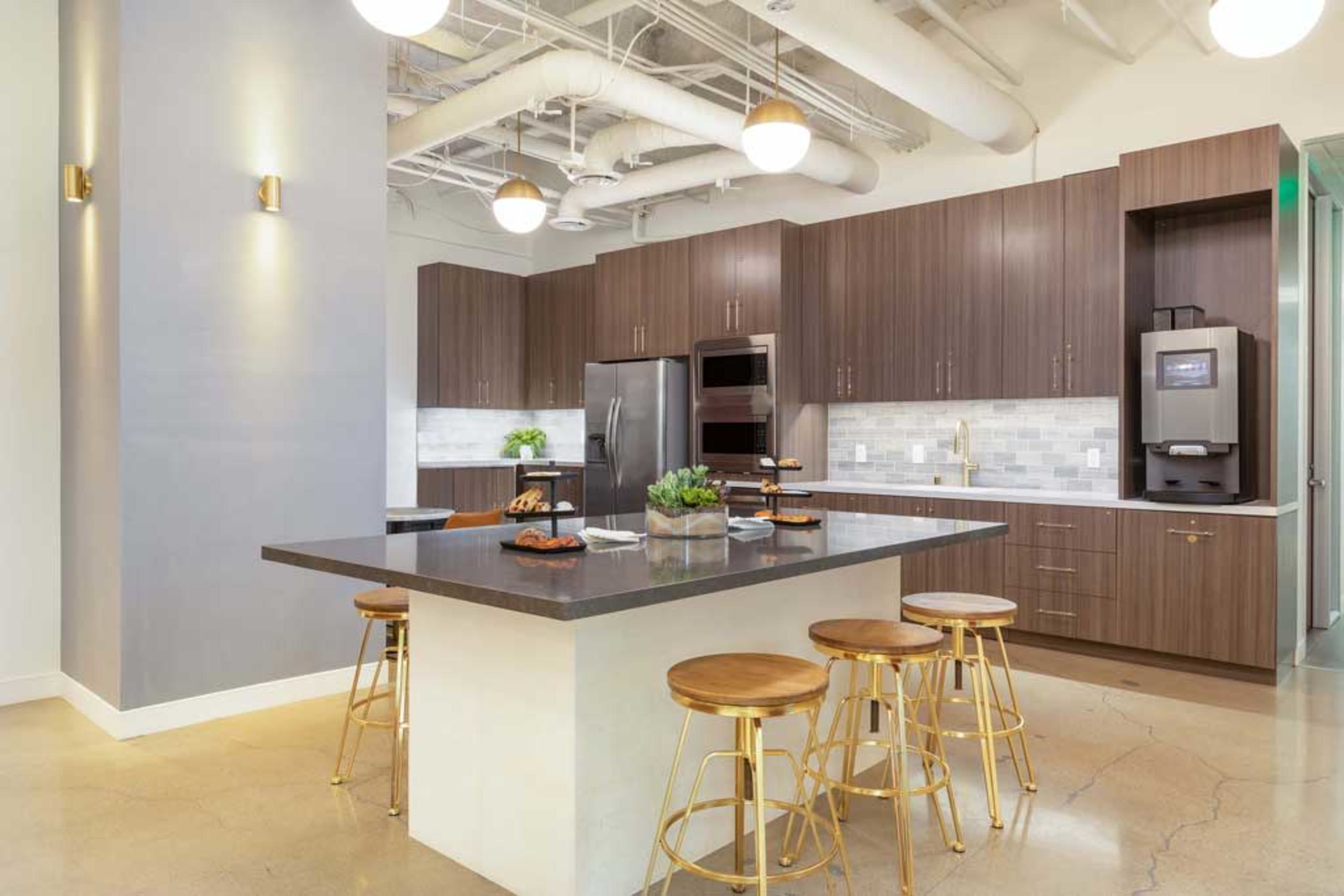 A modern kitchen with dark wooden cabinetry, a central island, and four golden barstools, illuminated by hanging light fixtures.
