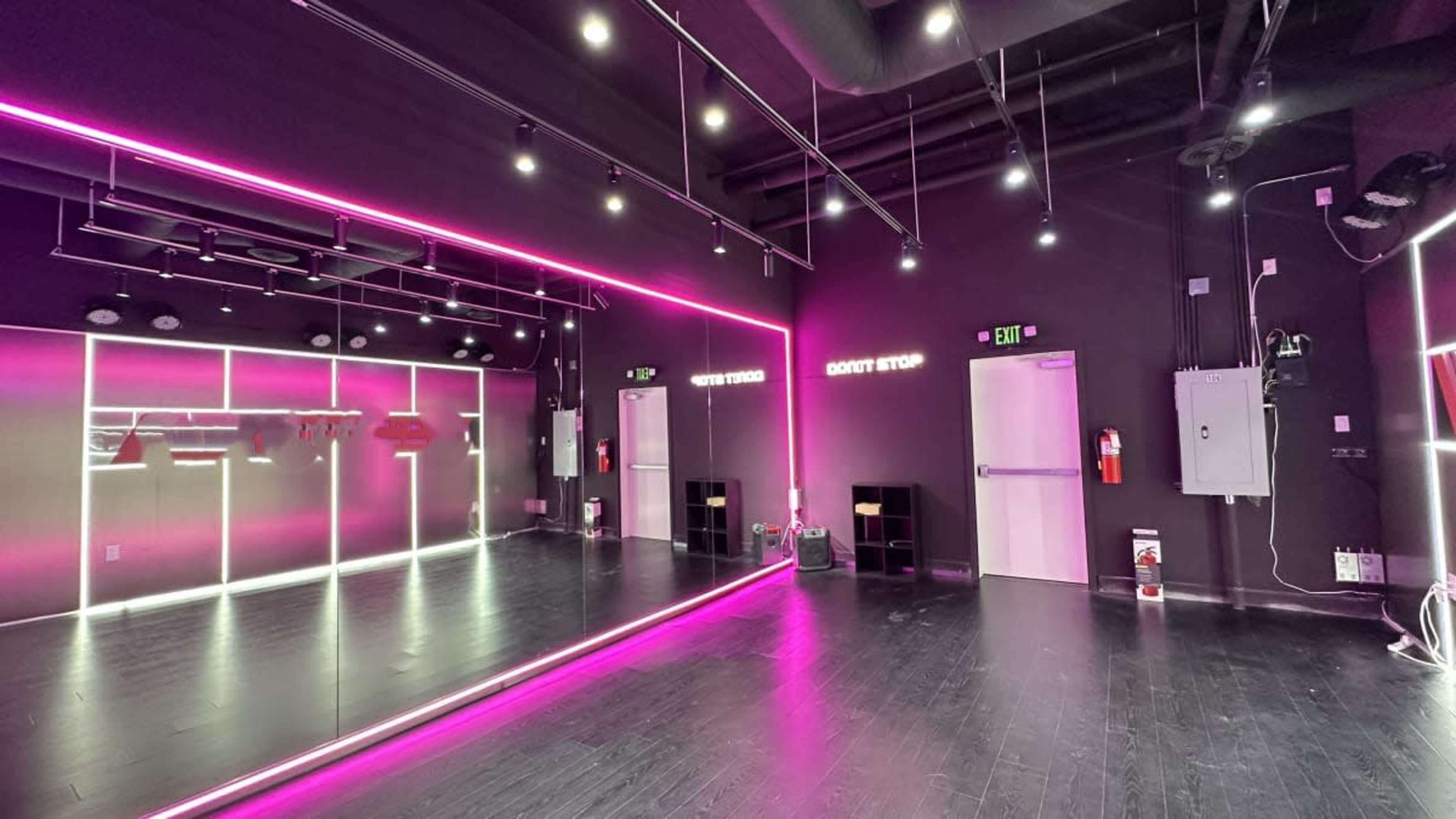 The interior of a modern fitness studio features black walls, mirrored surfaces, and vibrant pink LED lighting.