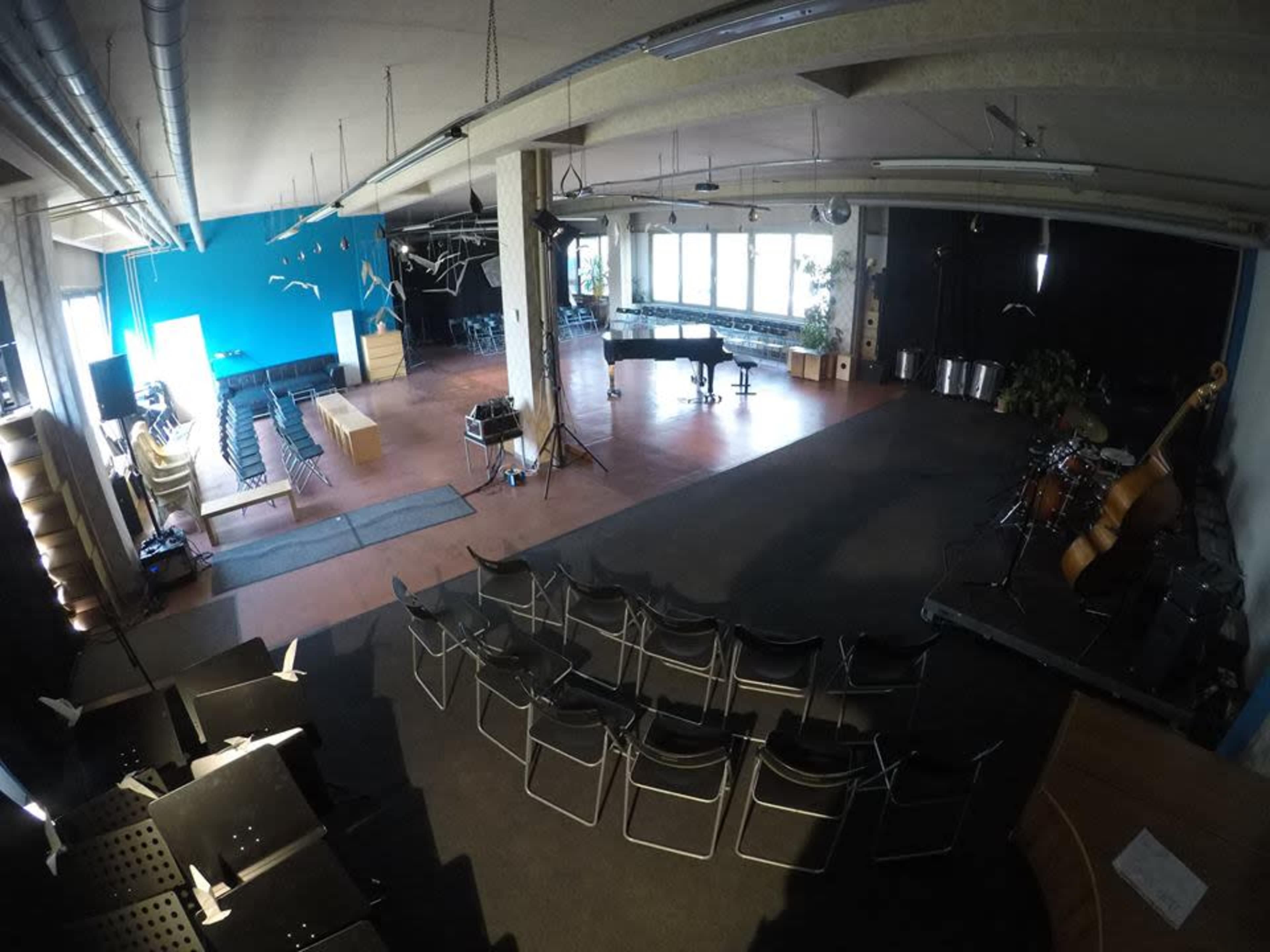 A spacious performance venue featuring a grand piano, a small stage with musical instruments, and rows of black chairs arranged for an audience.