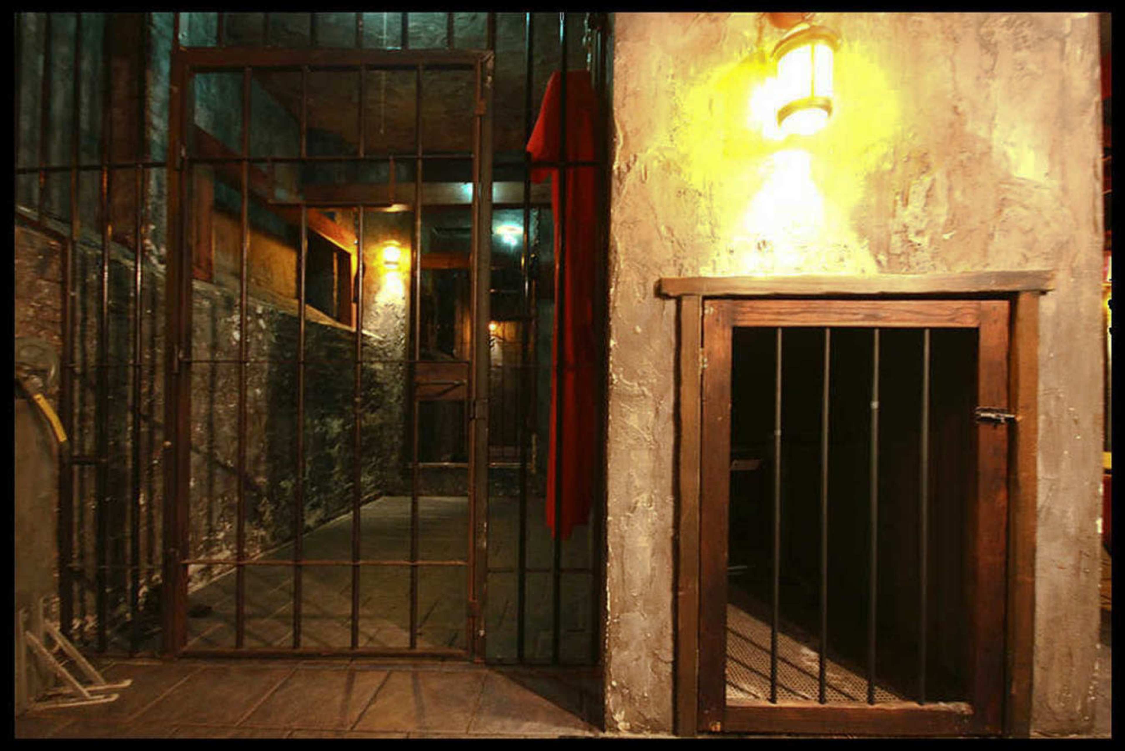 The image shows a dimly lit, enclosed space with barred gates and a small, locked entrance on the right.