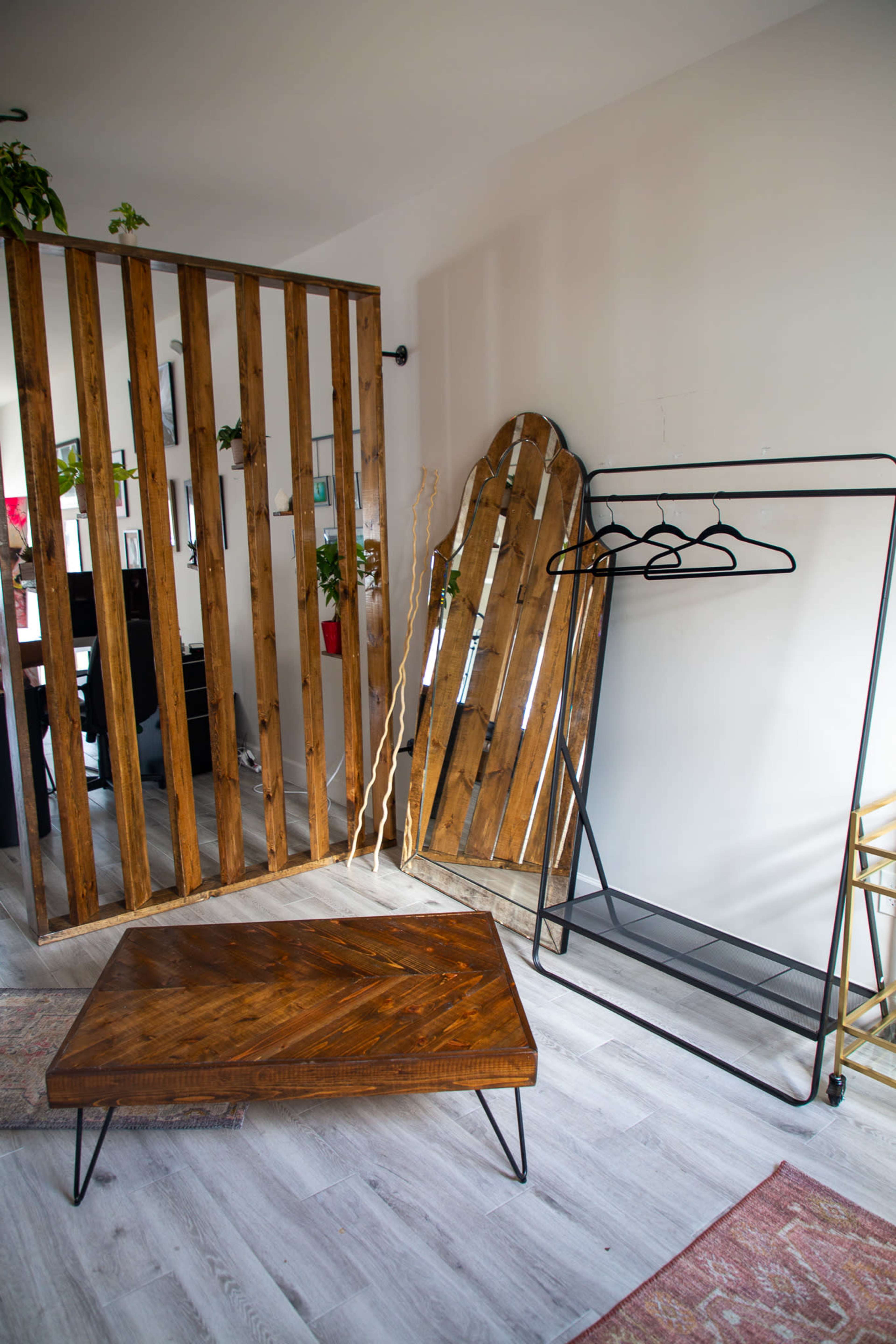 A modern living space featuring a wooden slat partition, a large mirror, a minimalist clothing rack, and a low wooden coffee table.