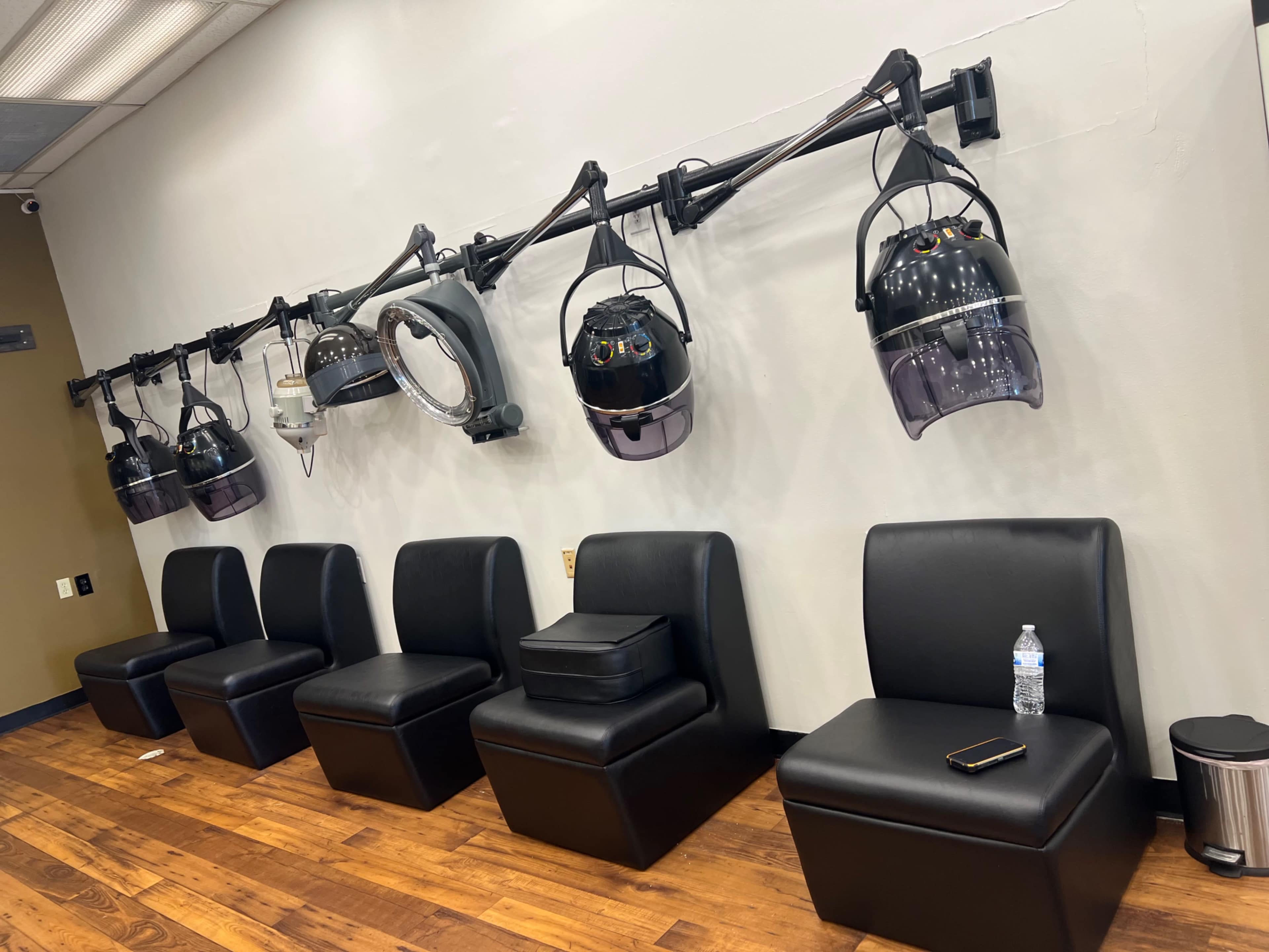 A row of salon chairs along a wall, equipped with multiple overhead hair drying units.