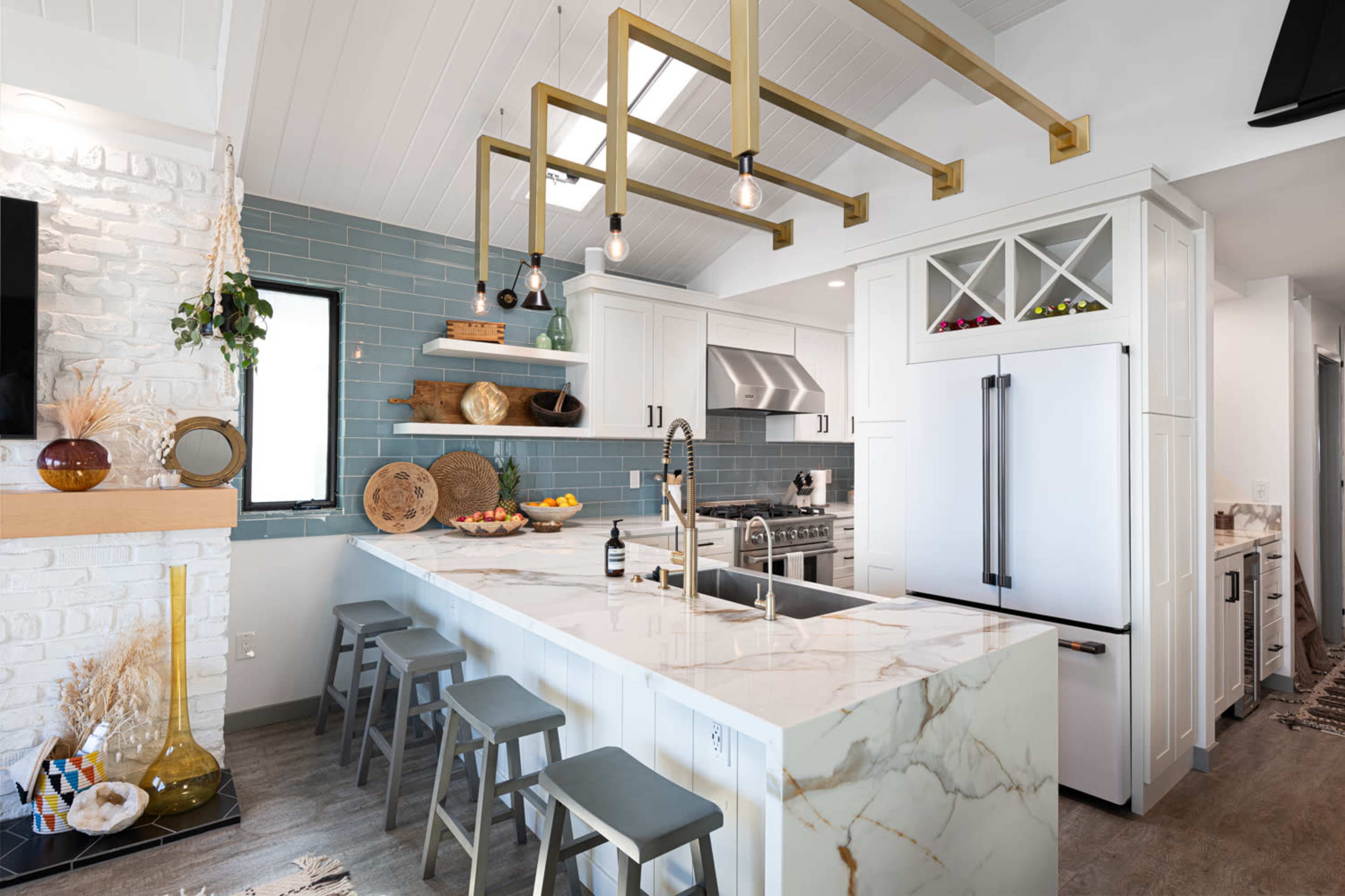 A modern kitchen features a large marble island with bar stools, stainless steel appliances, and blue tiled walls.