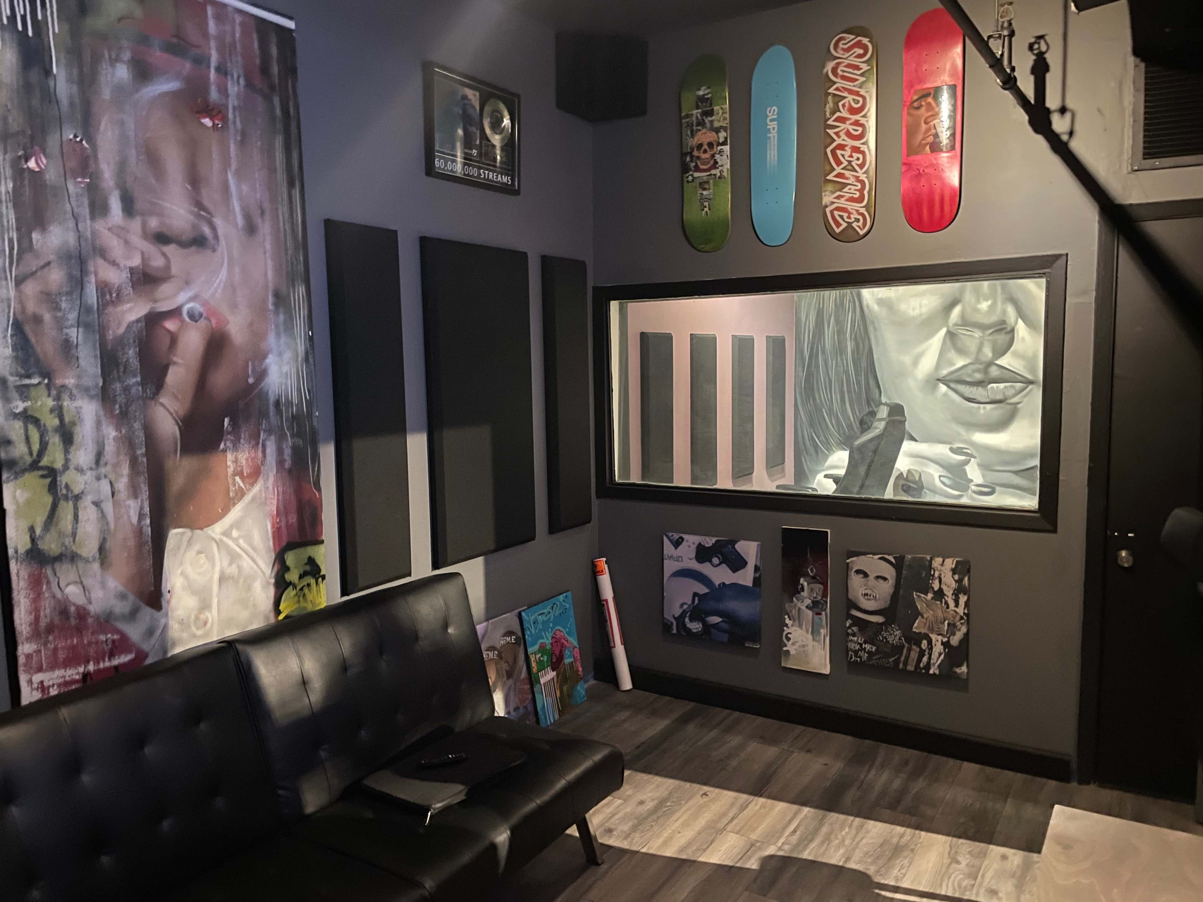 A modern lounge area with a black couch, walls adorned with various artworks, and a window displaying a large monochromatic drawing.