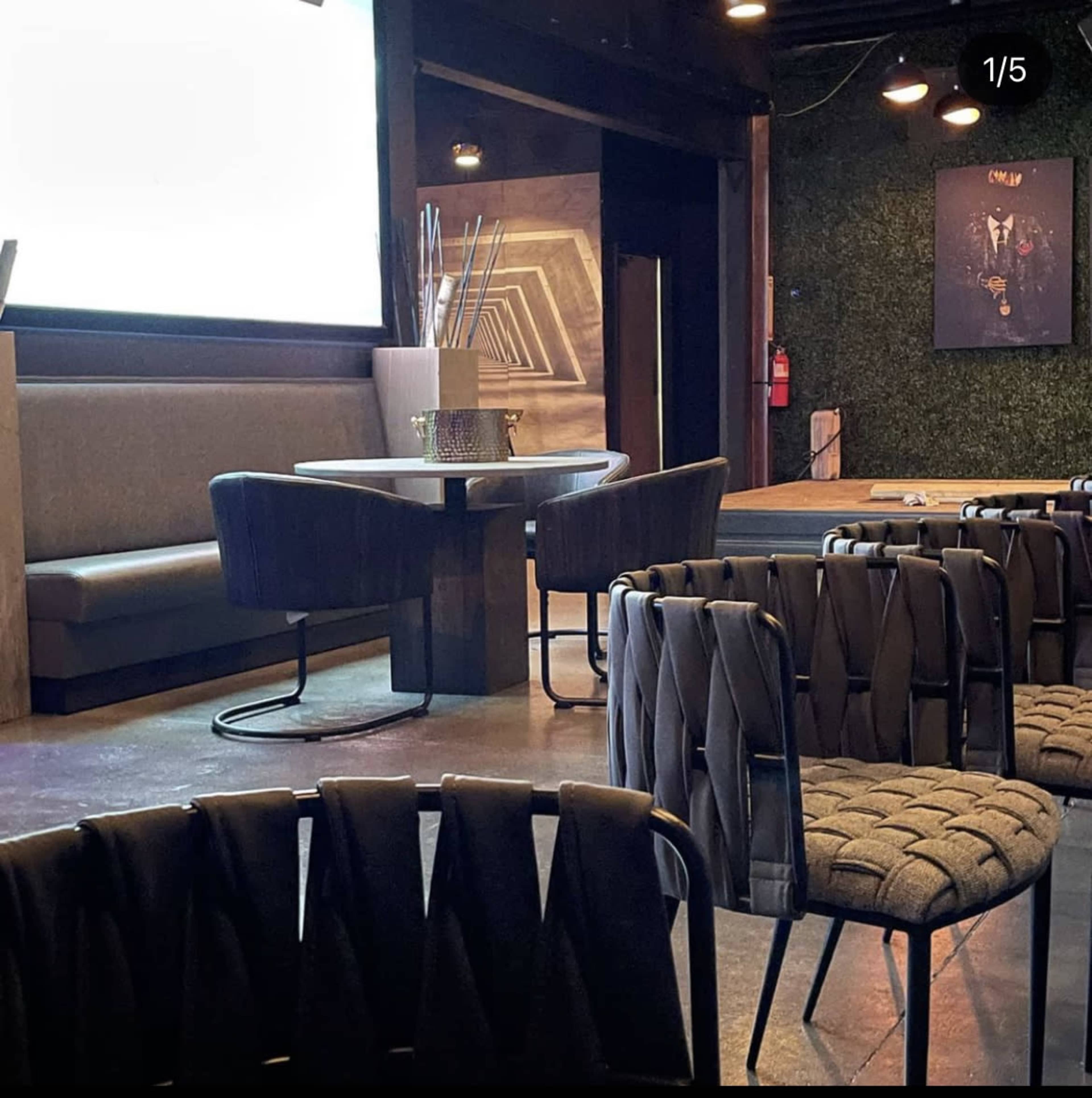 A modern interior of a venue featuring a seating area with a round table, an upholstered bench, and stylish woven chairs.
