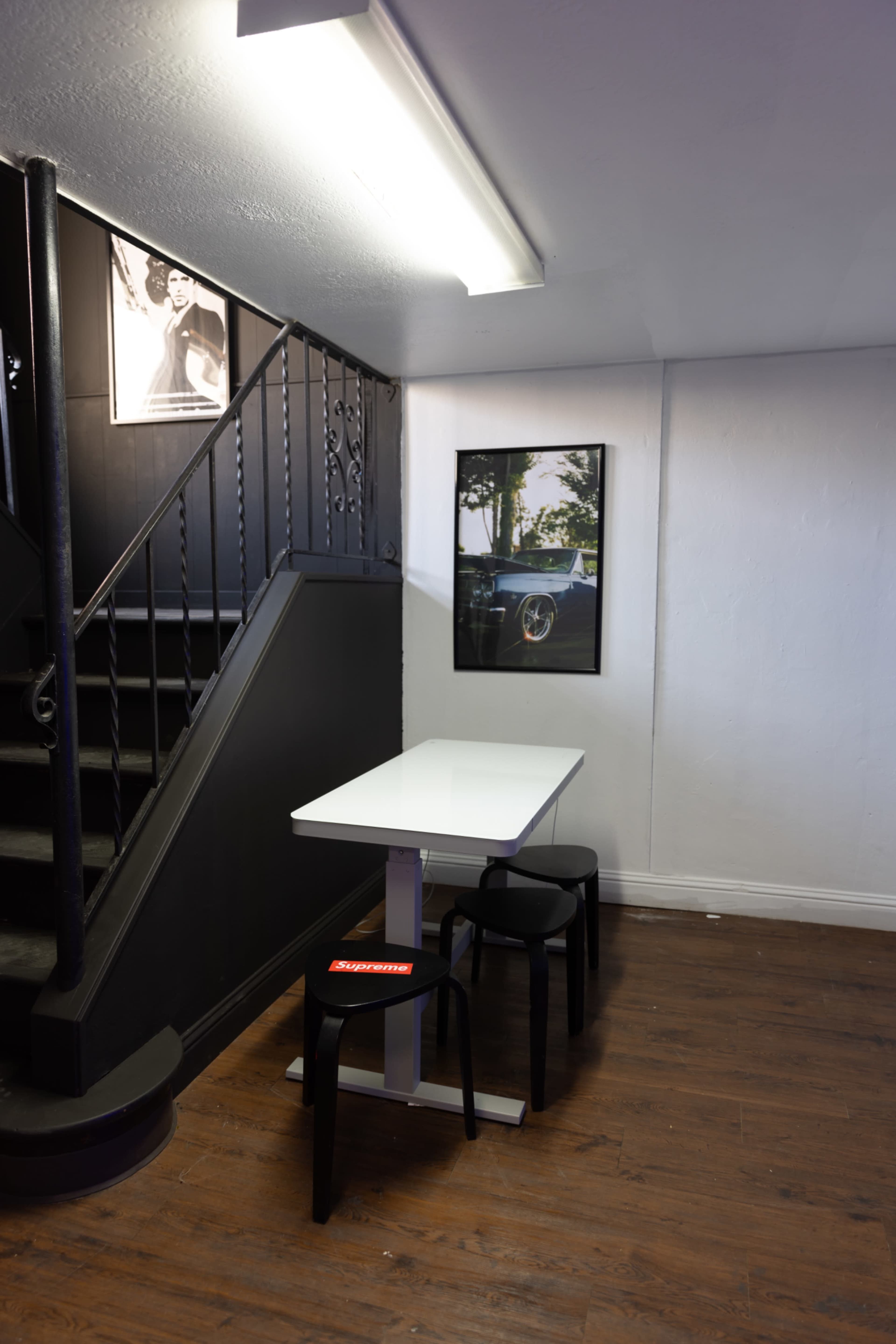 A small eating area features a white table and two black chairs beside a staircase, with framed photographs on the walls.