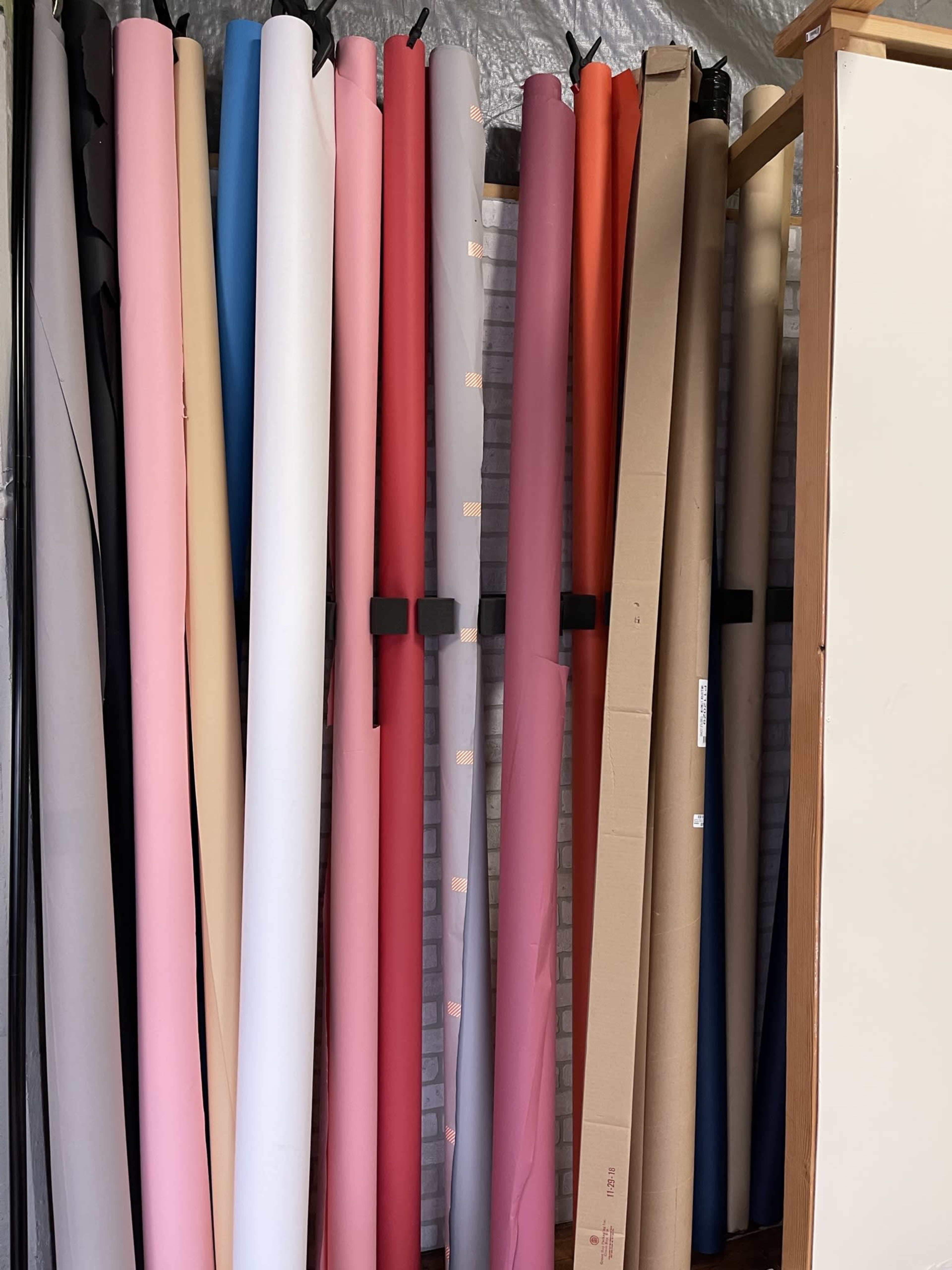 A collection of rolled paper sheets in various colors stored upright between a wall and a wooden structure.