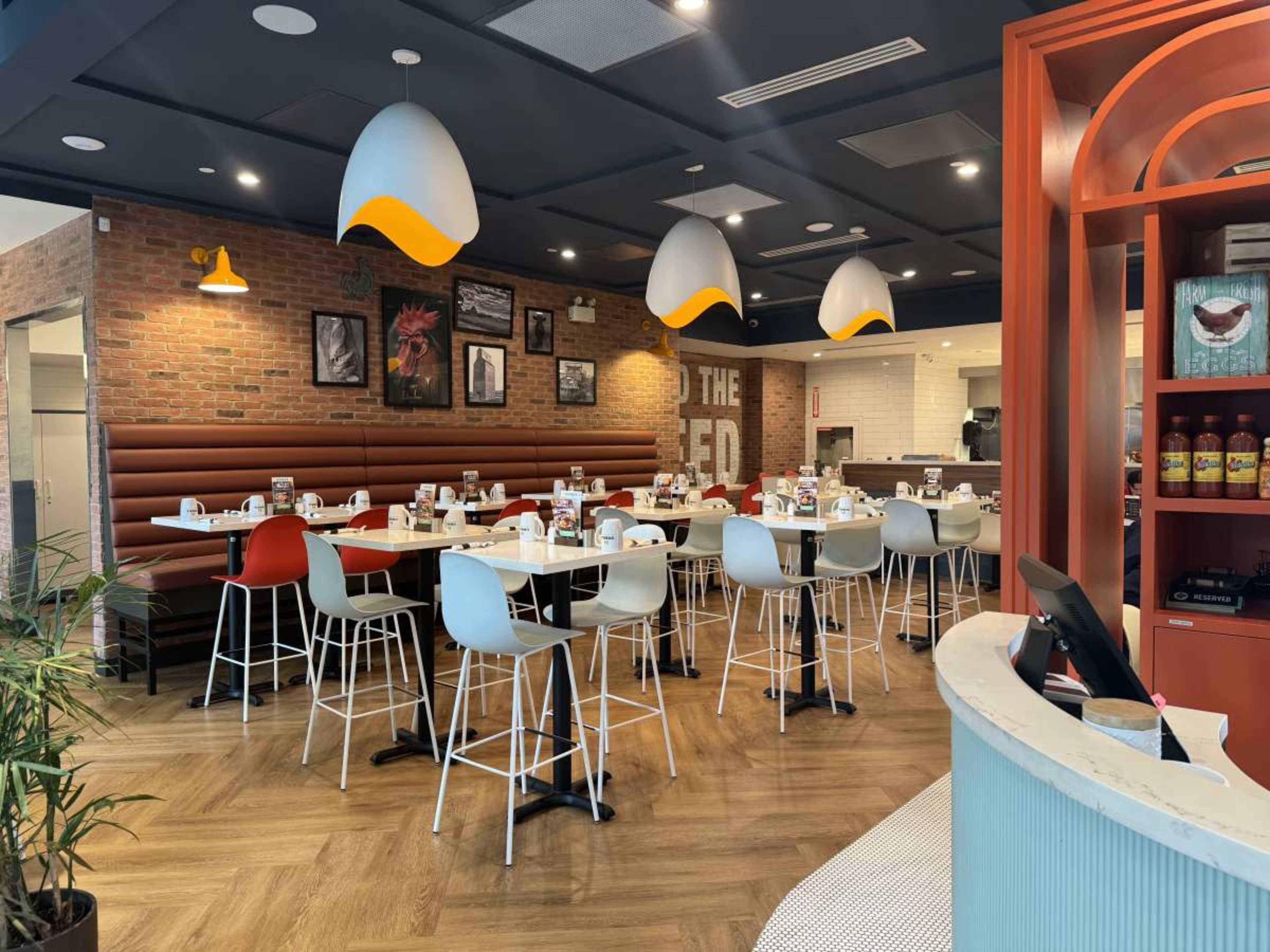 The image shows a modern restaurant interior with wooden flooring, a mix of seating options, and pendant lighting.