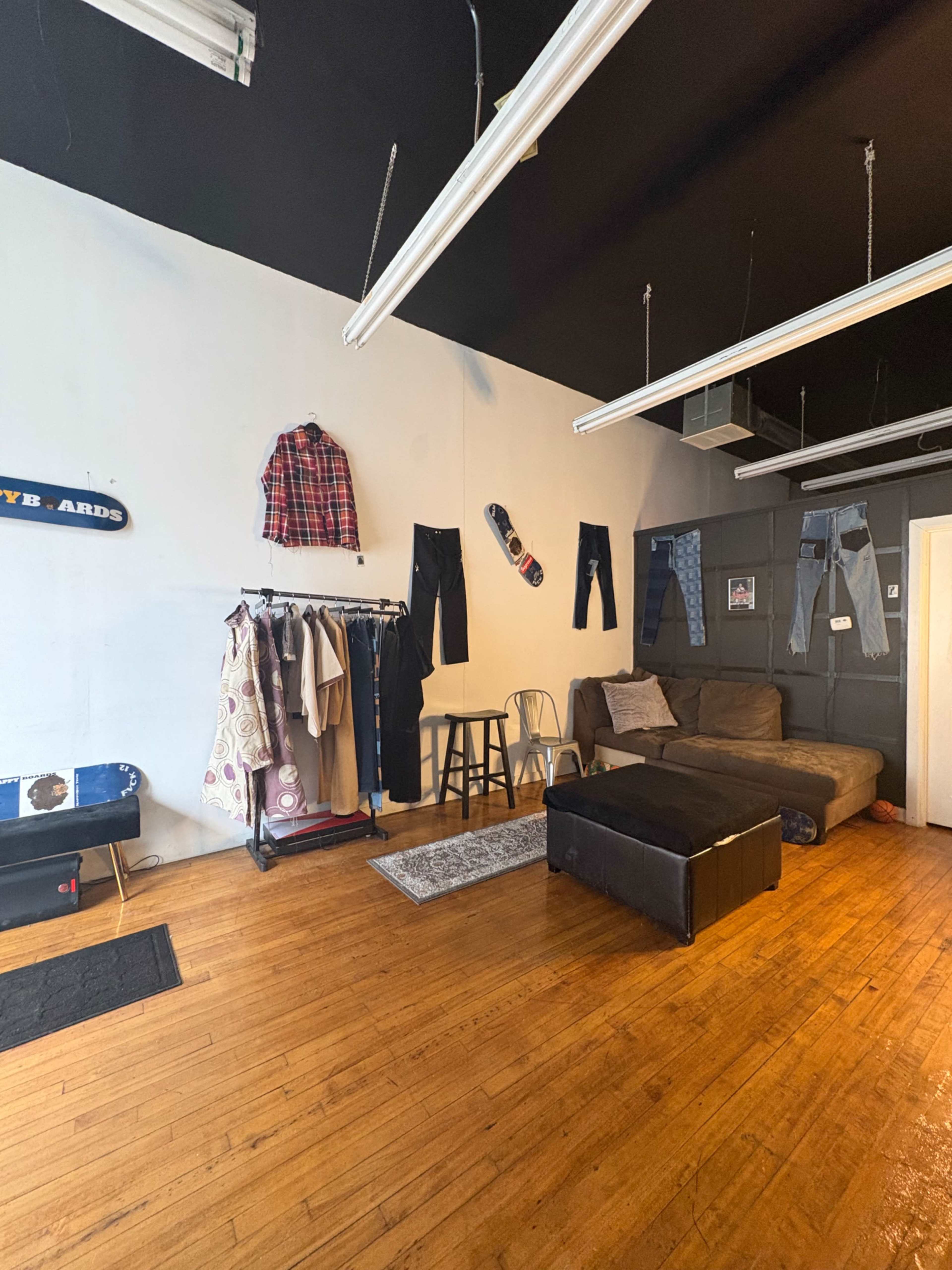 The image shows a minimalist clothing store interior with hanging clothes, a couch, a small table, and skateboard decor on the walls.