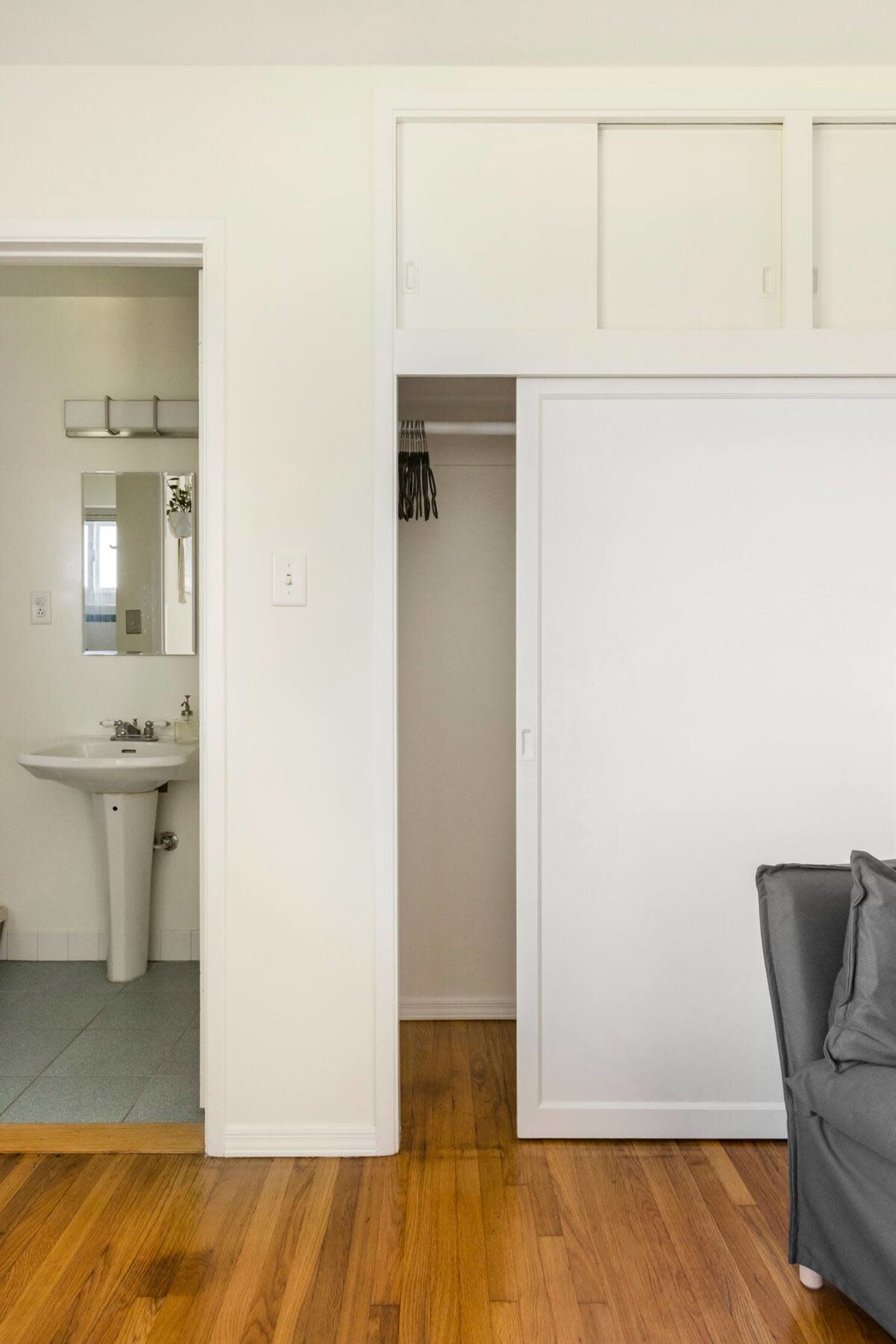 A bathroom entrance on the left and a closet with sliding doors on the right, adjacent to a living area with a gray couch.