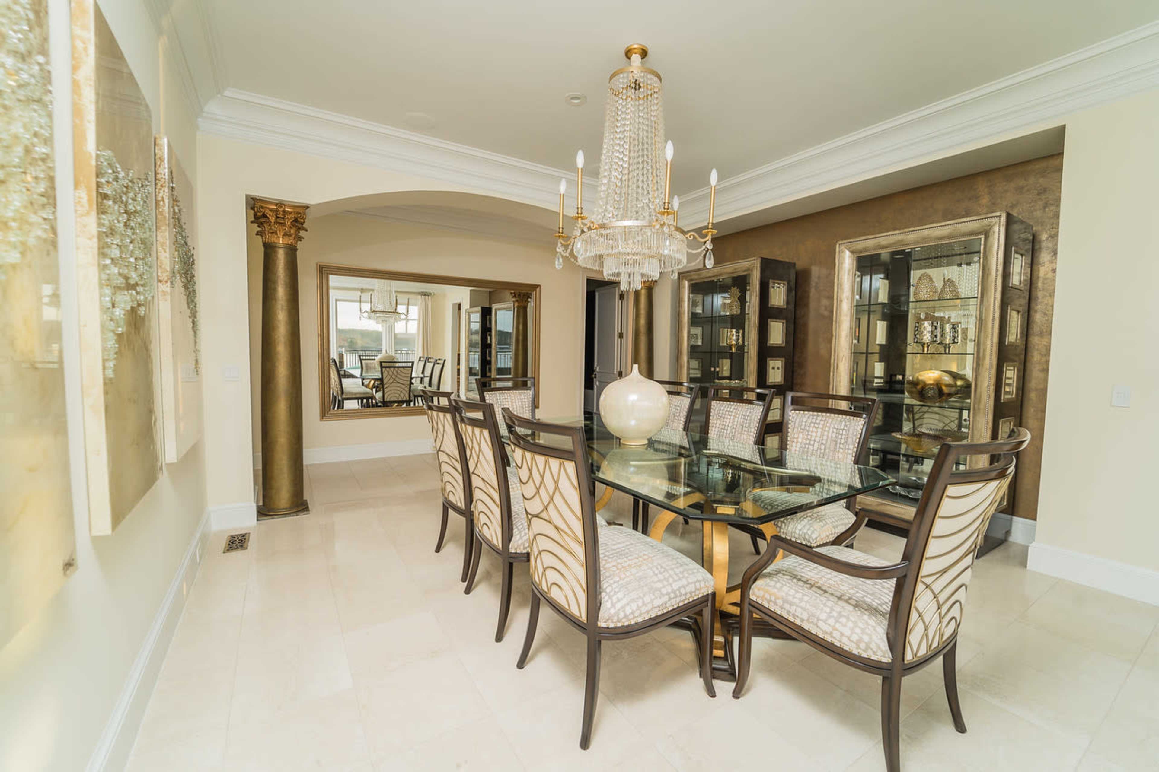 A spacious dining room featuring a glass dining table surrounded by upholstered chairs, a large chandelier, and decorative mirrors on the walls.