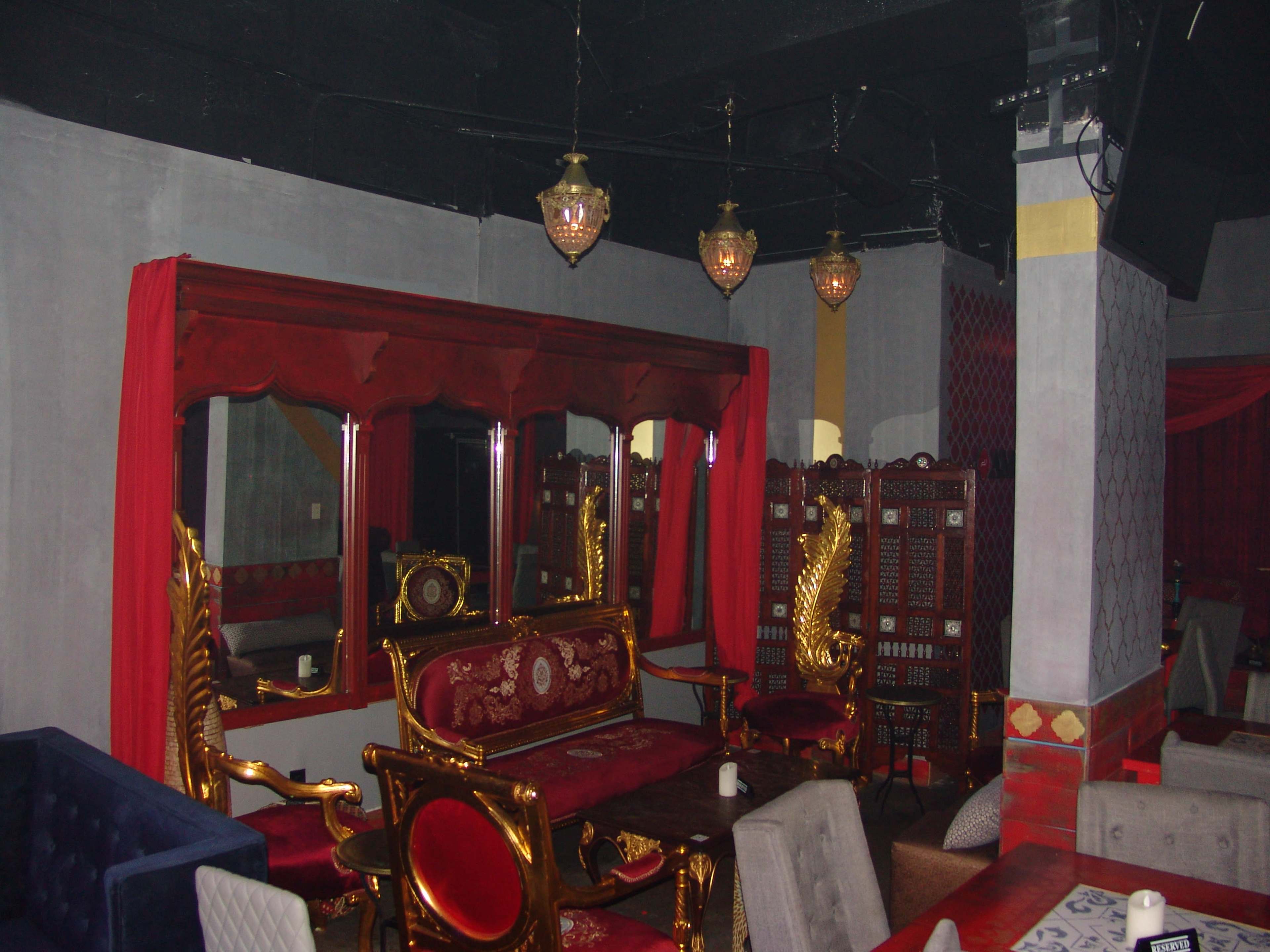 The image shows a dimly lit lounge with ornate golden furniture, colorful drapery, and decorative screens along the walls.