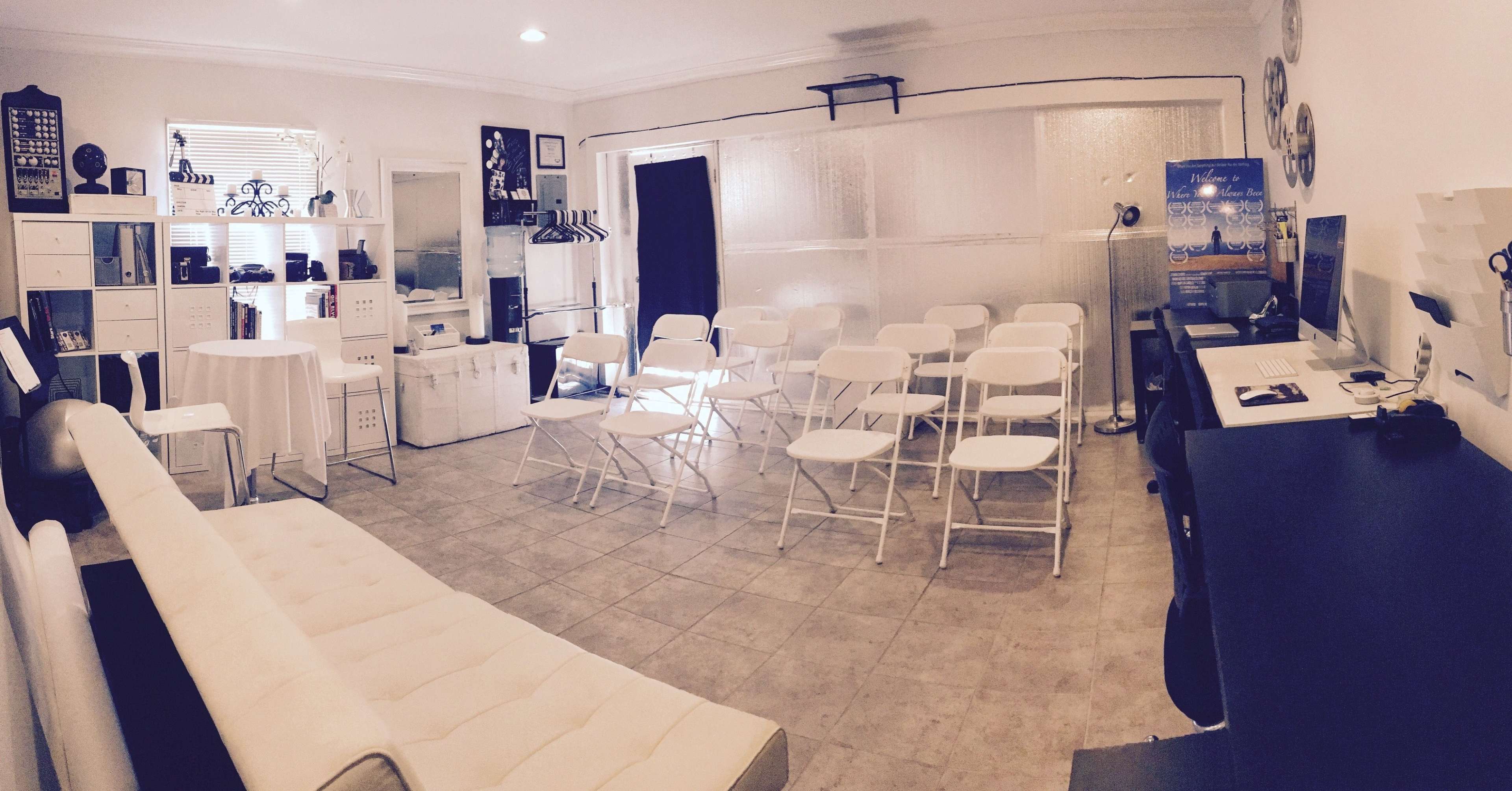 A meeting room set up with a row of white folding chairs facing a table and a wall with various items displayed.