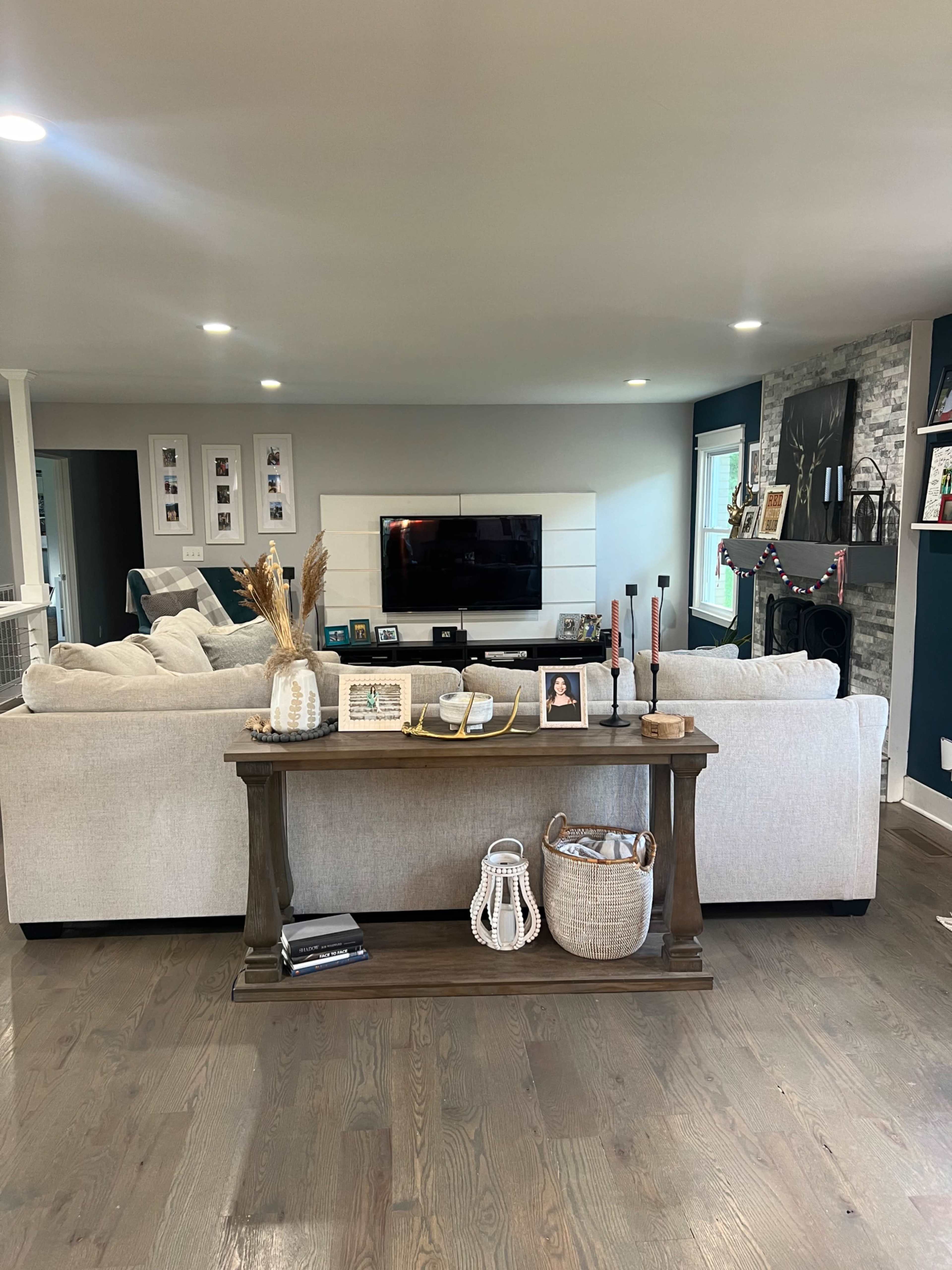 A light-colored sectional sofa faces a sleek television mounted on a white wall, with decorative items and a console table in front of it.