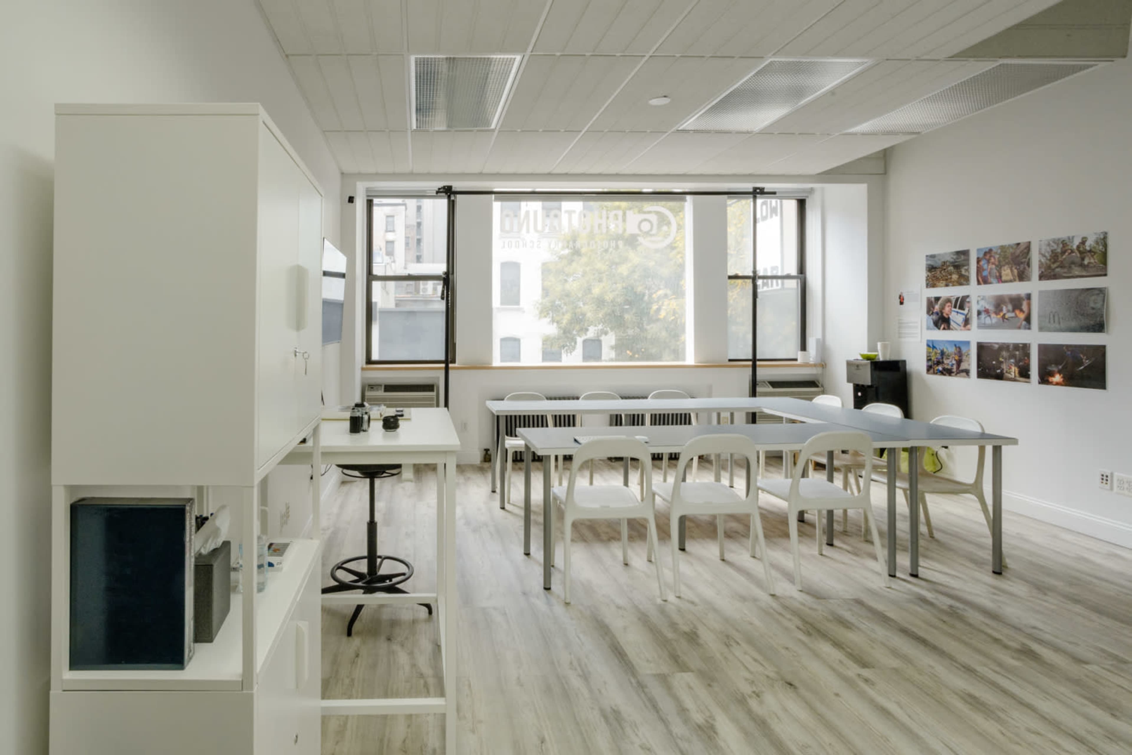 The image shows a modern, minimalist meeting room featuring a long table with chairs, a white cabinet, and several framed pictures on the wall.