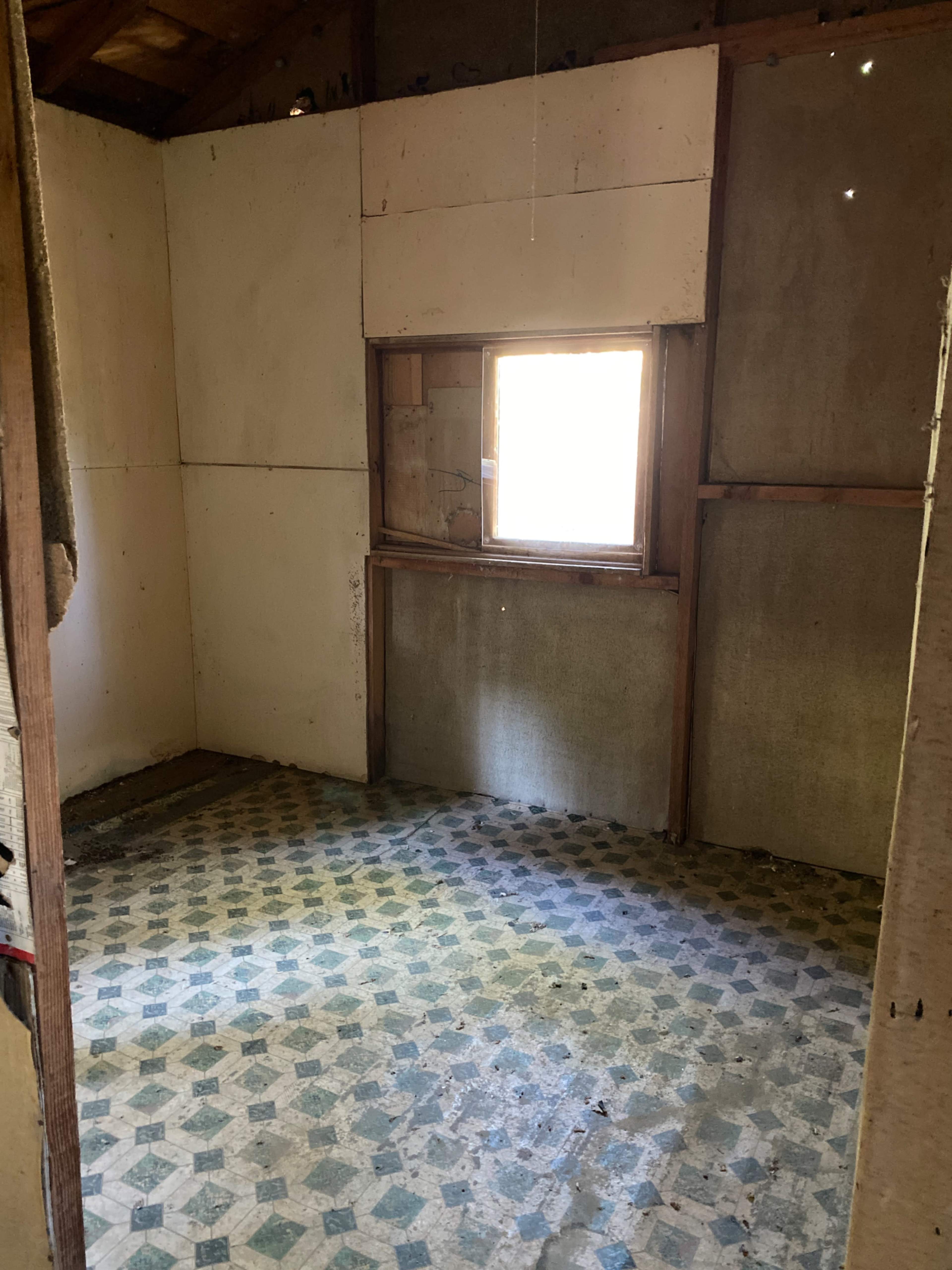 The image shows a vacant room with a window, bare walls, and a patterned floor.