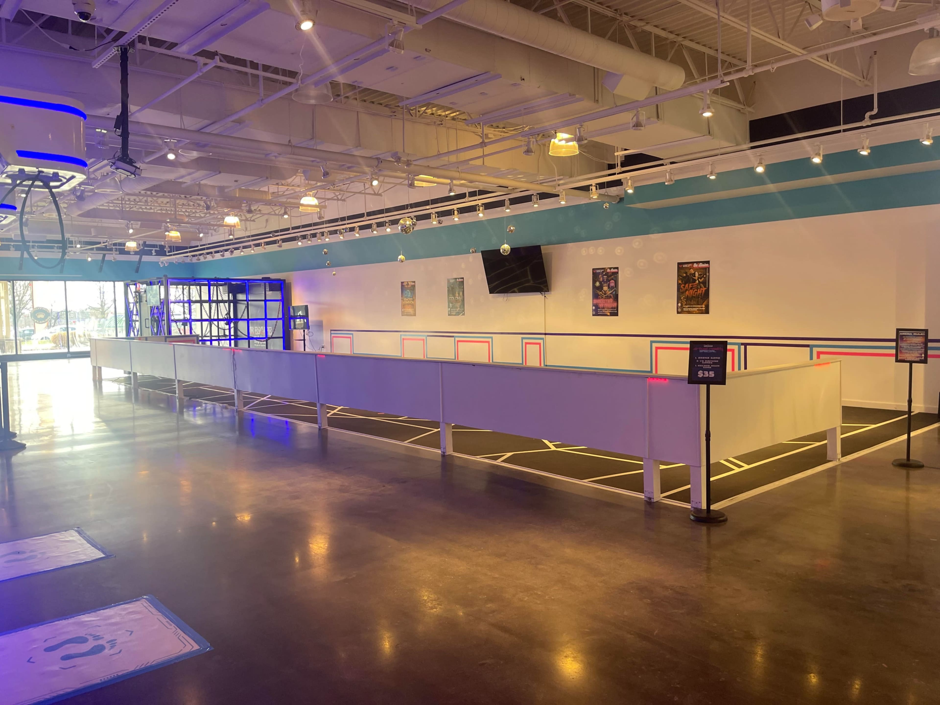 An empty indoor entertainment space with a racetrack layout, surrounded by barriers and featuring colorful lighting and poster decorations on the walls.