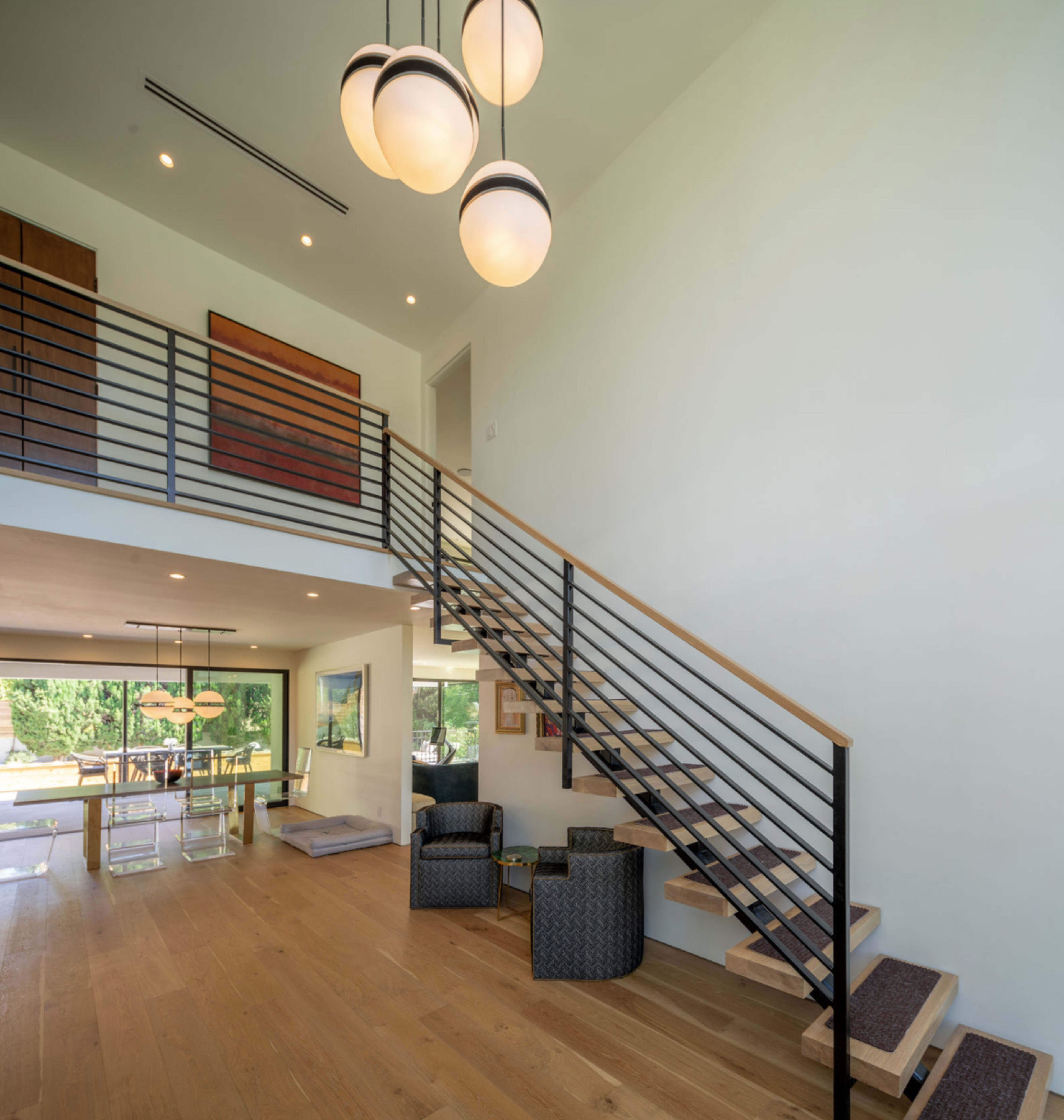 A modern interior space with a wood and metal staircase leading to an upper level, accompanied by contemporary lighting fixtures and minimalistic furnishings.