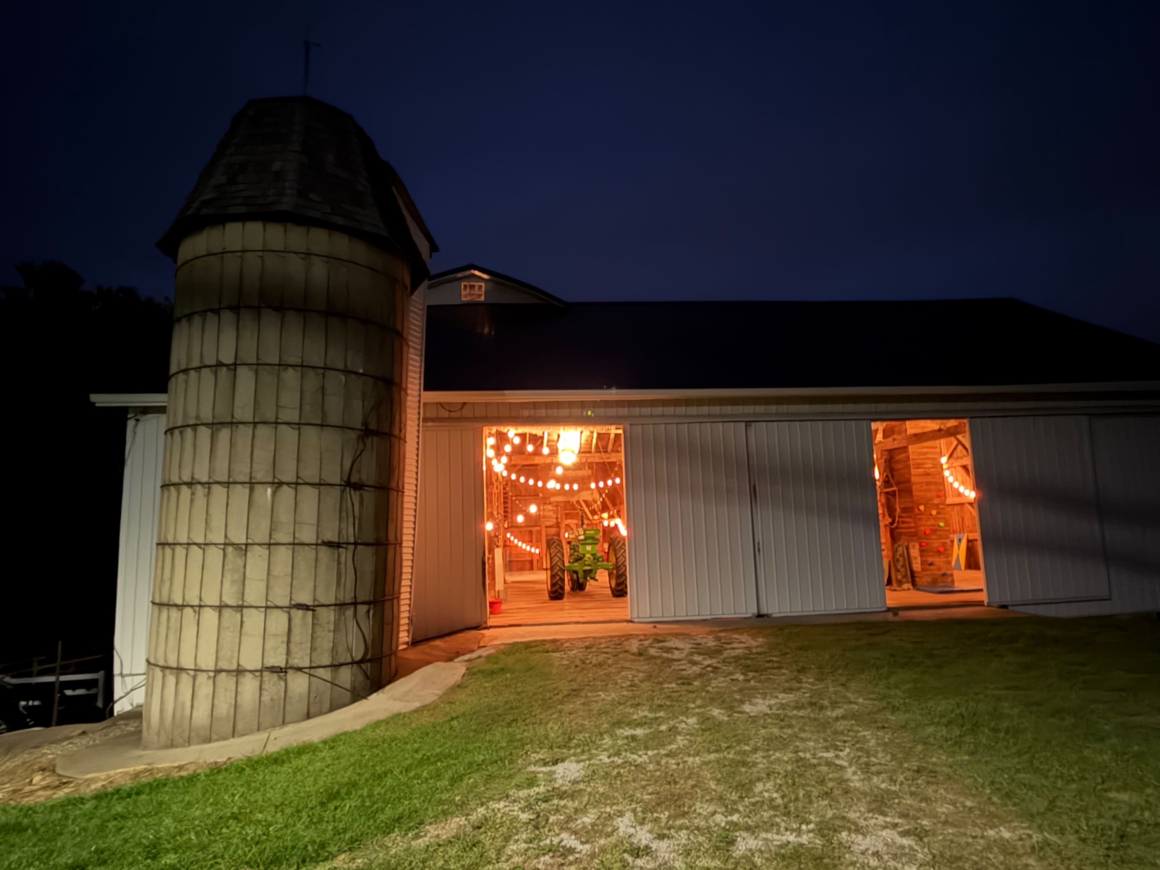 A barn with a silo is illuminated by warm lights at night, creating a welcoming glow.