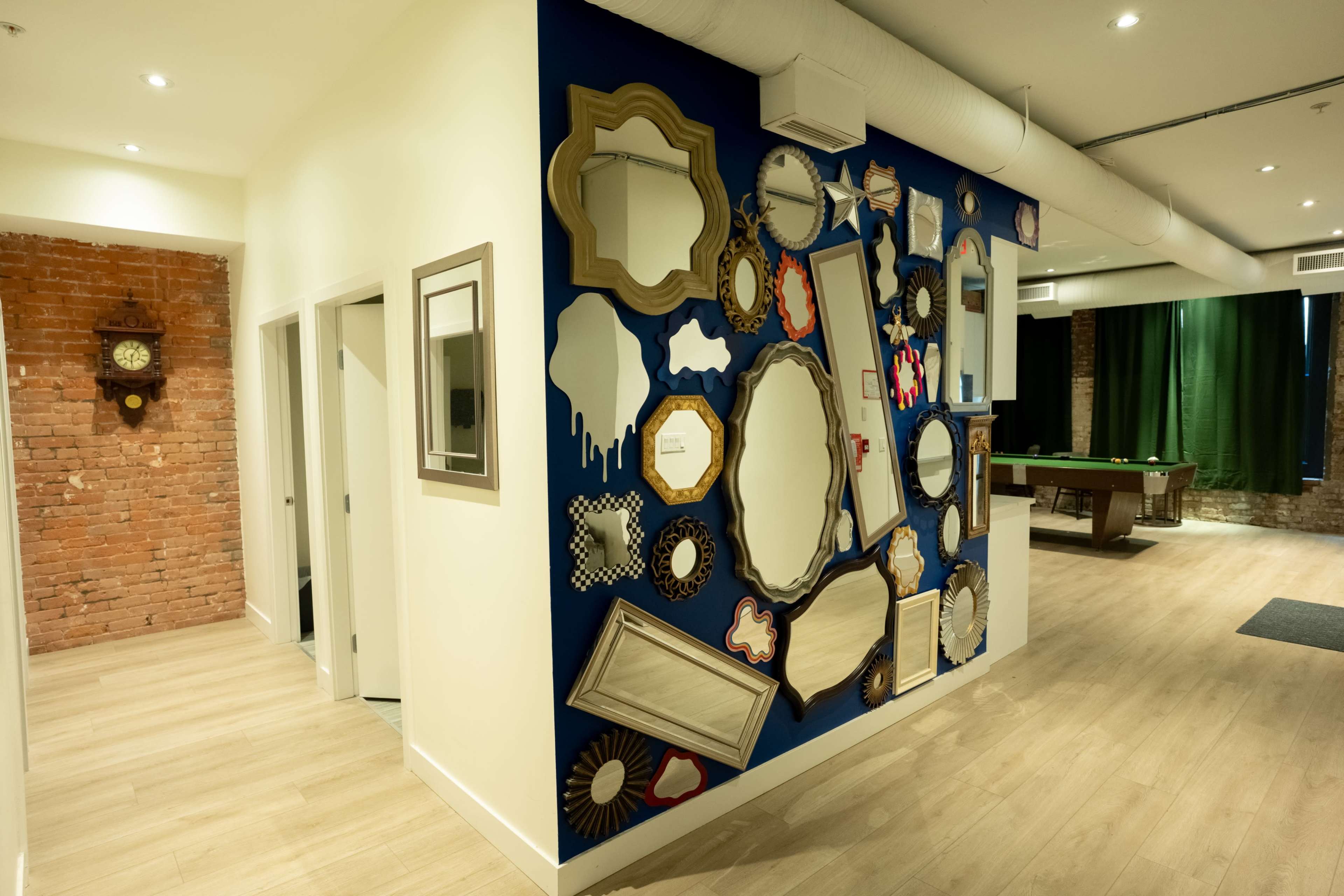 The image shows a hallway with a vibrant blue wall adorned with various decorative mirrors, and a clock mounted on a brick wall in the background.