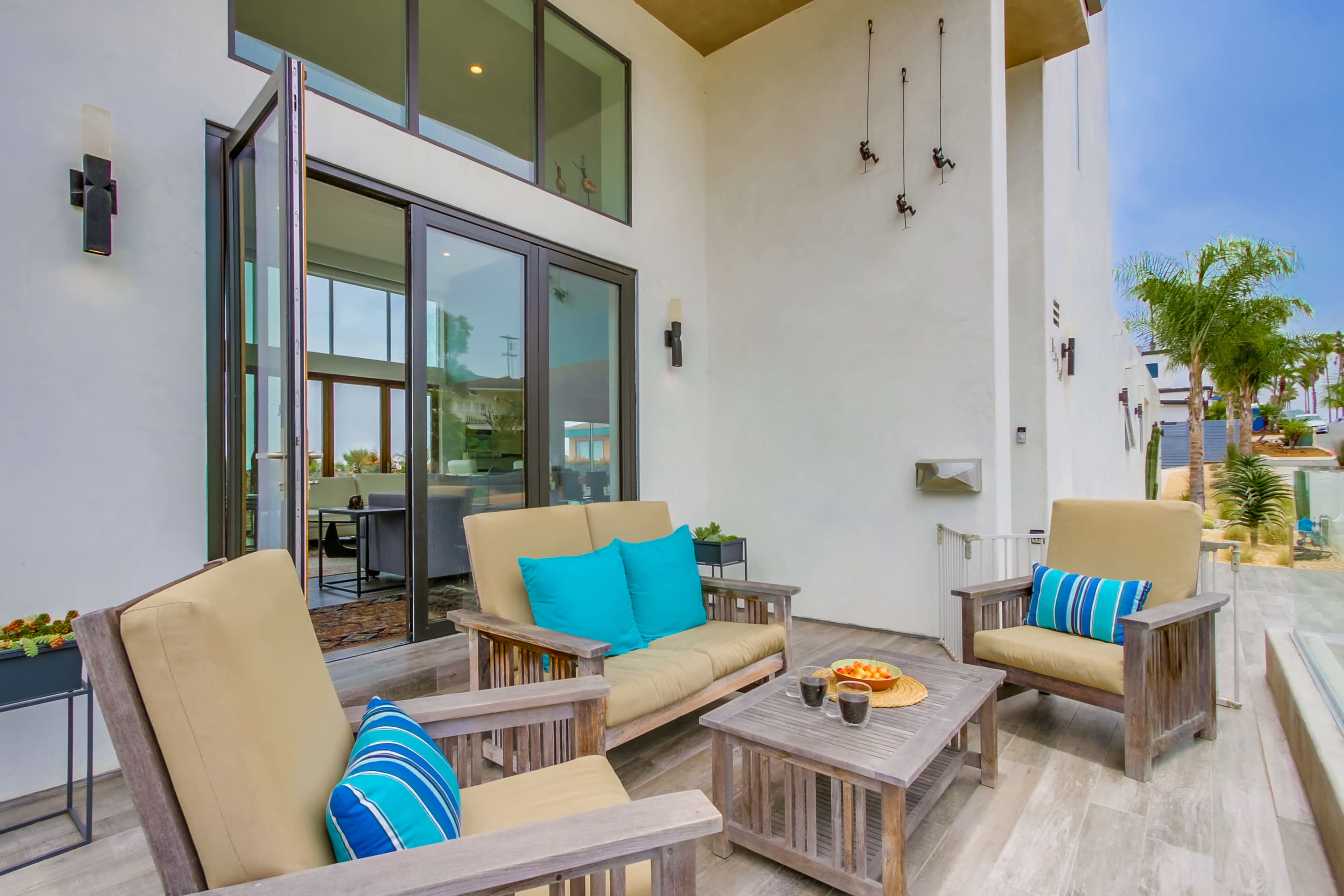 A modern outdoor seating area with two beige chairs and a coffee table, positioned on a patio adjacent to a large sliding glass door.