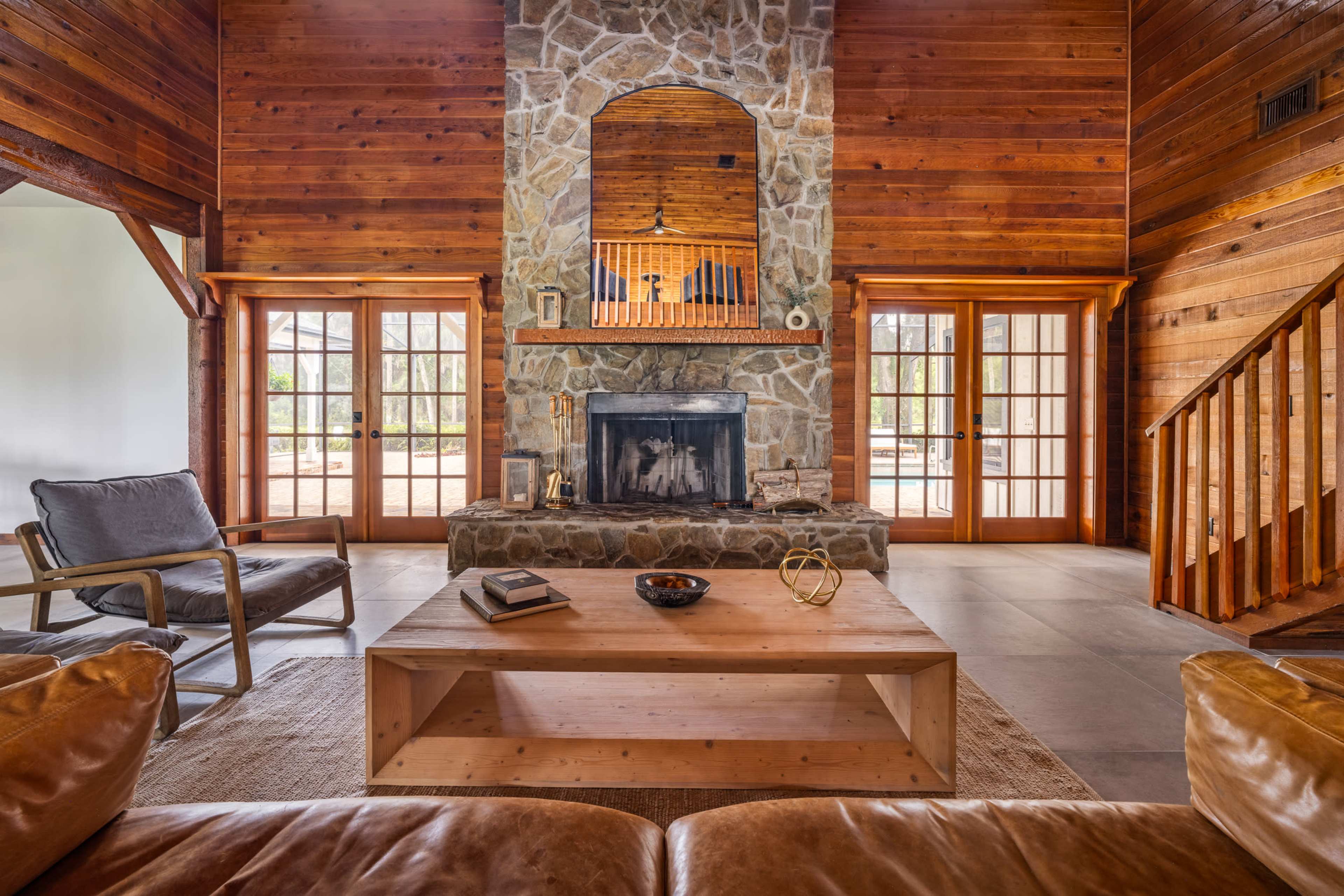 The living room features a stone fireplace with a wooden mantel, surrounded by a large wooden wall, and has large glass doors leading outside.
