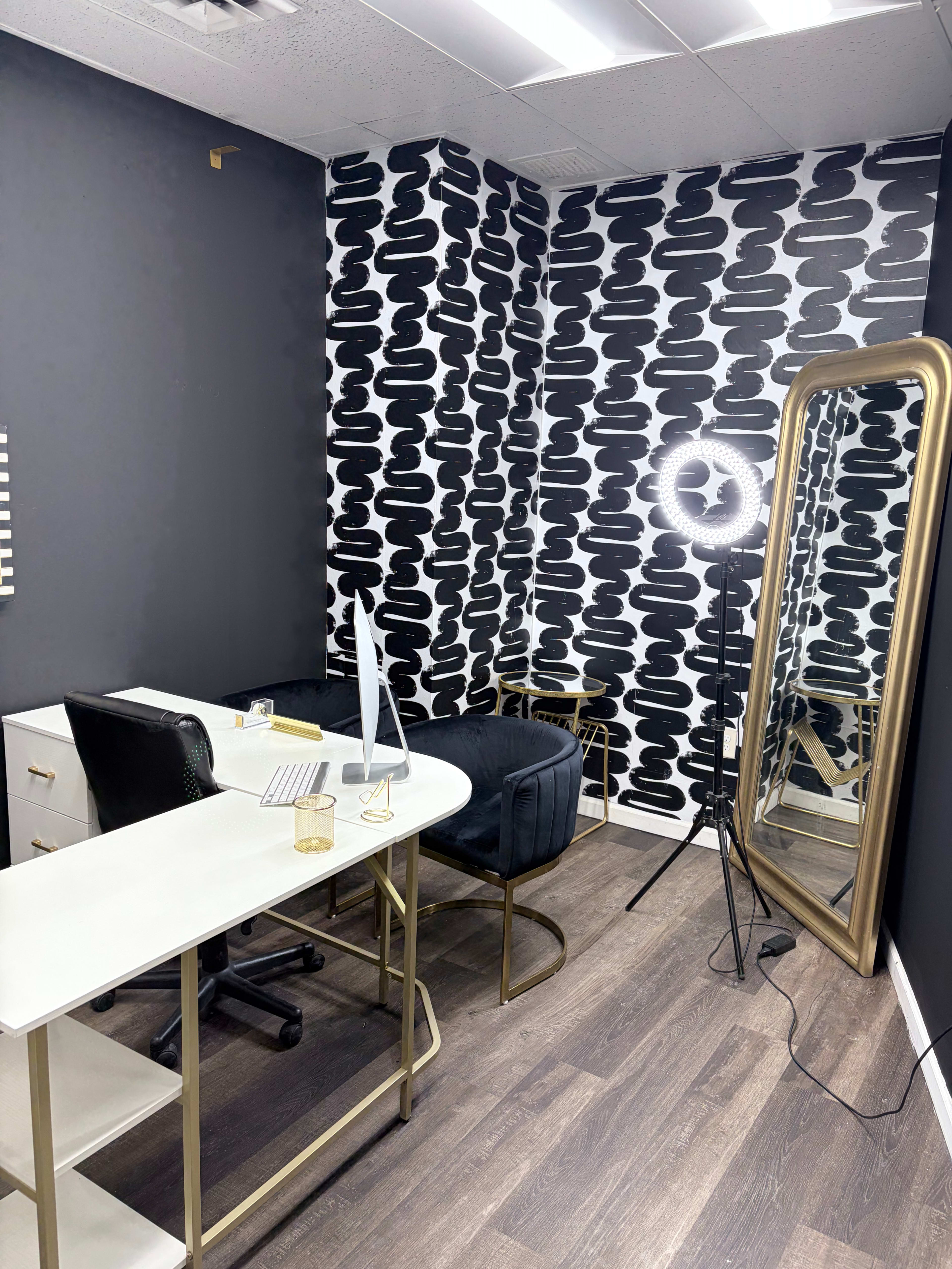 The image shows a modern office space featuring a desk with a computer, a black chair, a large mirror, and a patterned black and white accent wall.