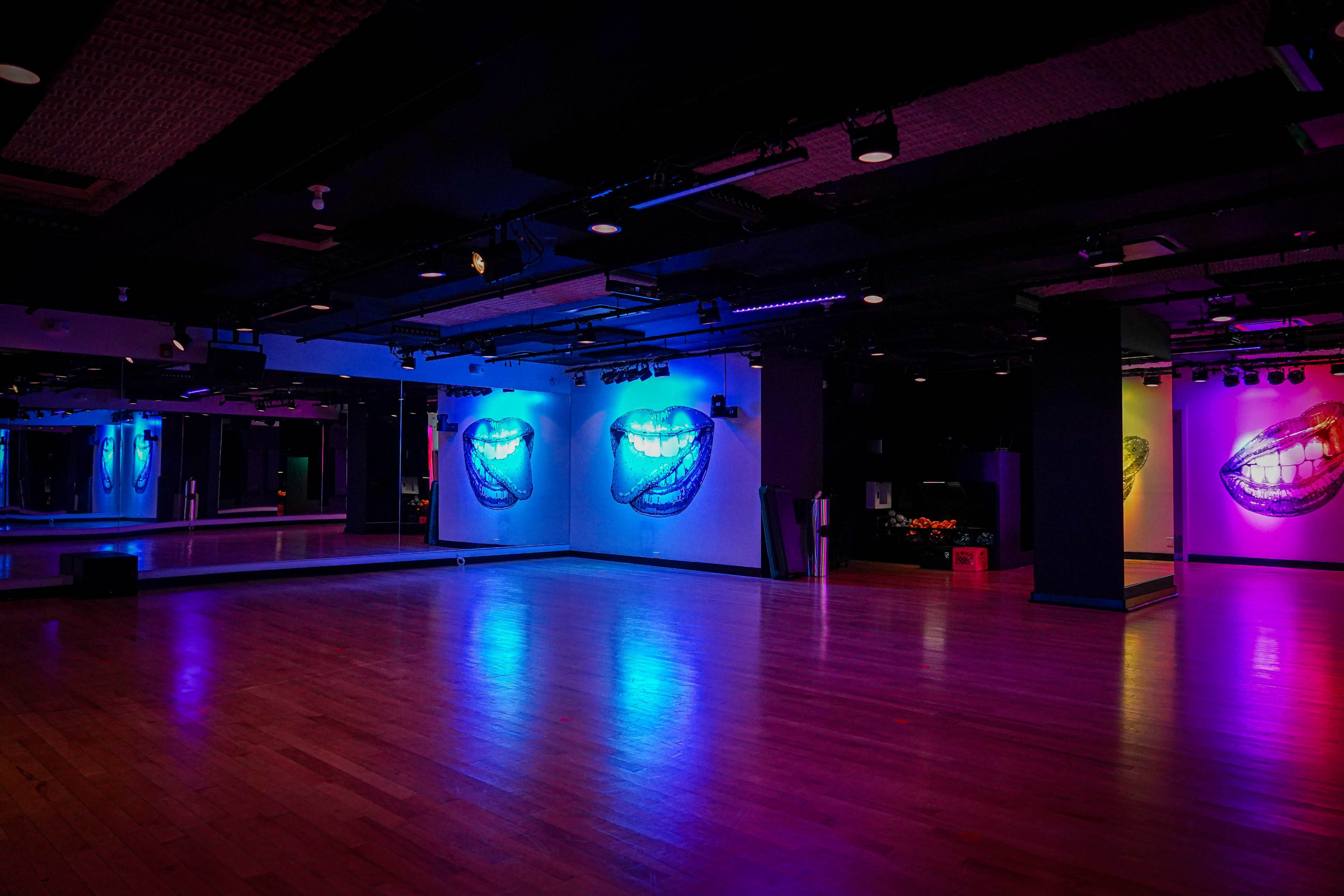 A spacious dance studio features colorful wall art of lips, highlighted by various lighting effects.