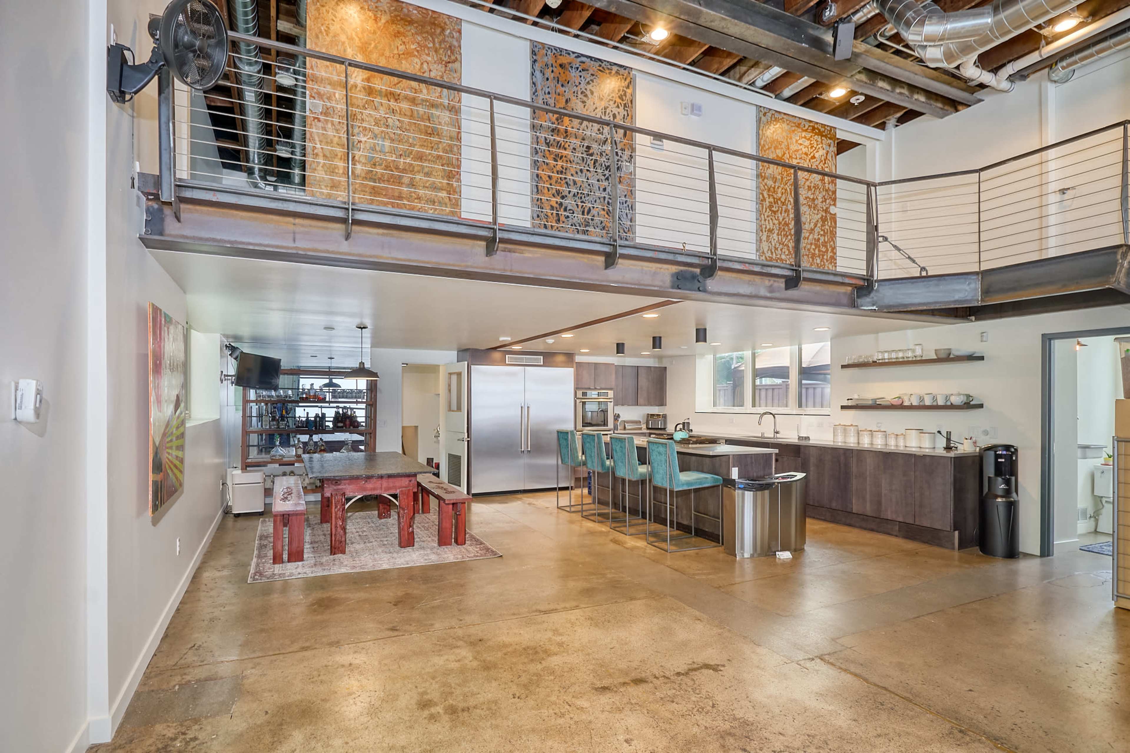 The image shows a modern open-concept kitchen and dining area with exposed wood beams, a large island with bar seating, and industrial-style decor.