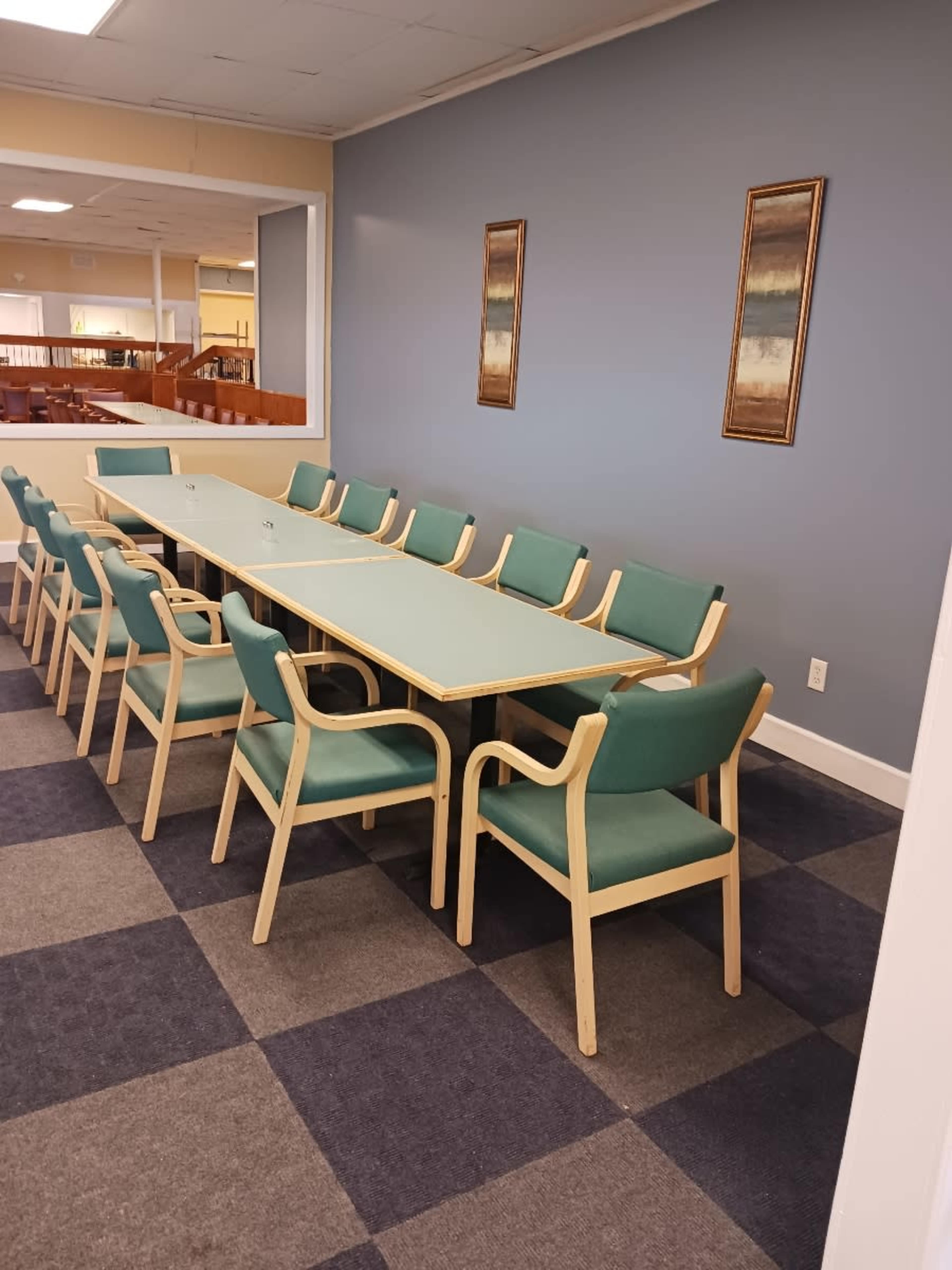 A long table with several chairs is set up in a room with gray walls and a carpeted floor.