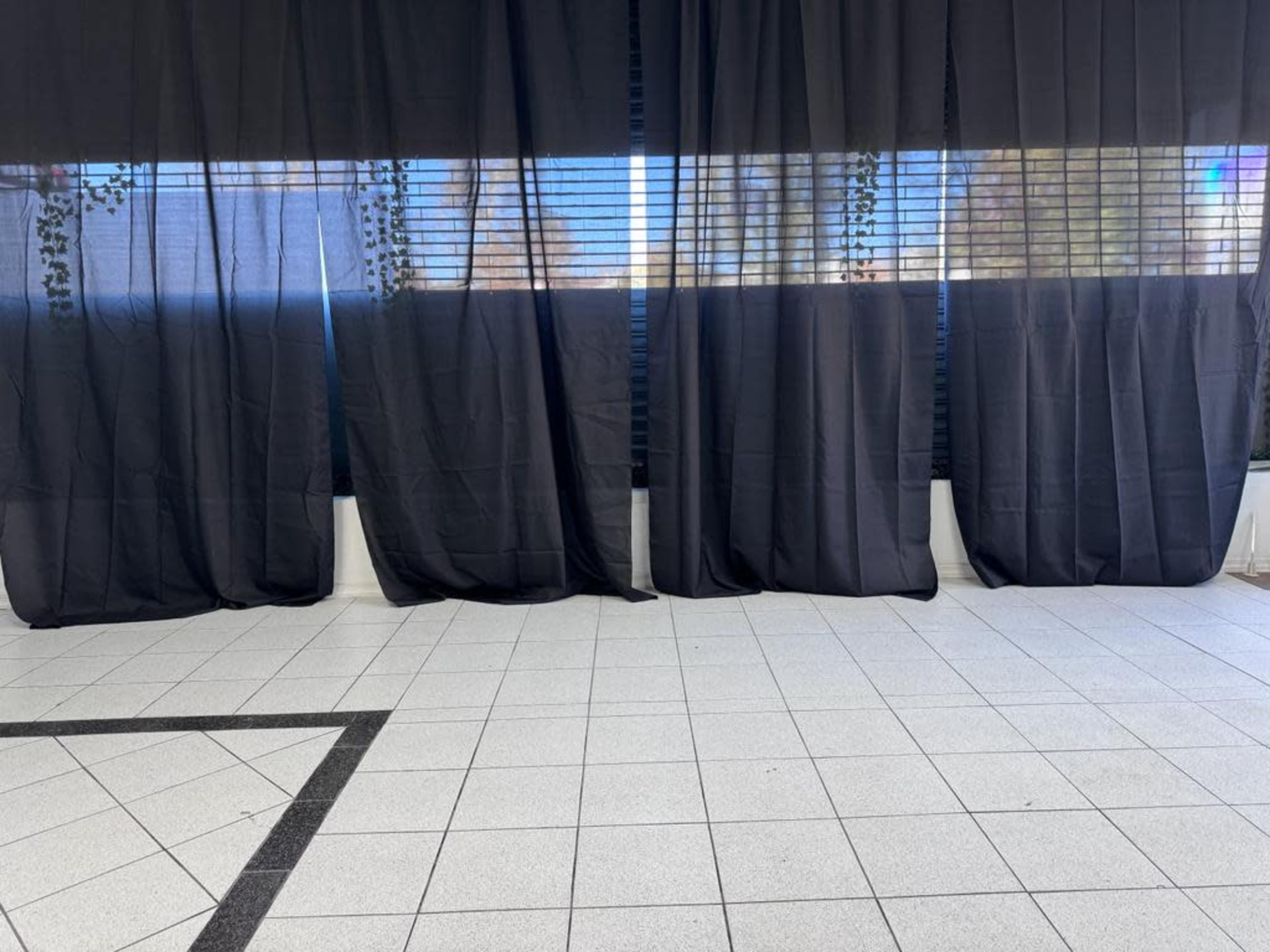 A room with tiled flooring and large black curtains covering windows.