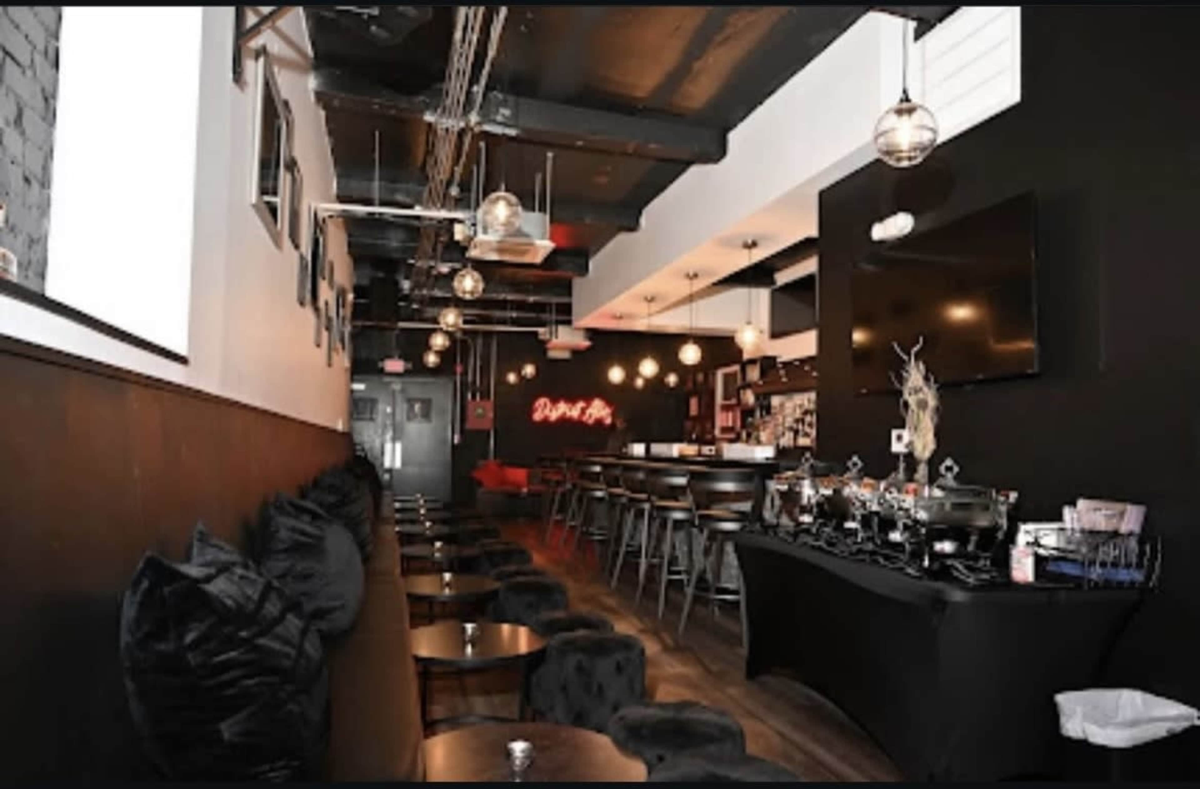 The image shows a modern restaurant interior with dark walls, plush seating, and stylish lighting fixtures.