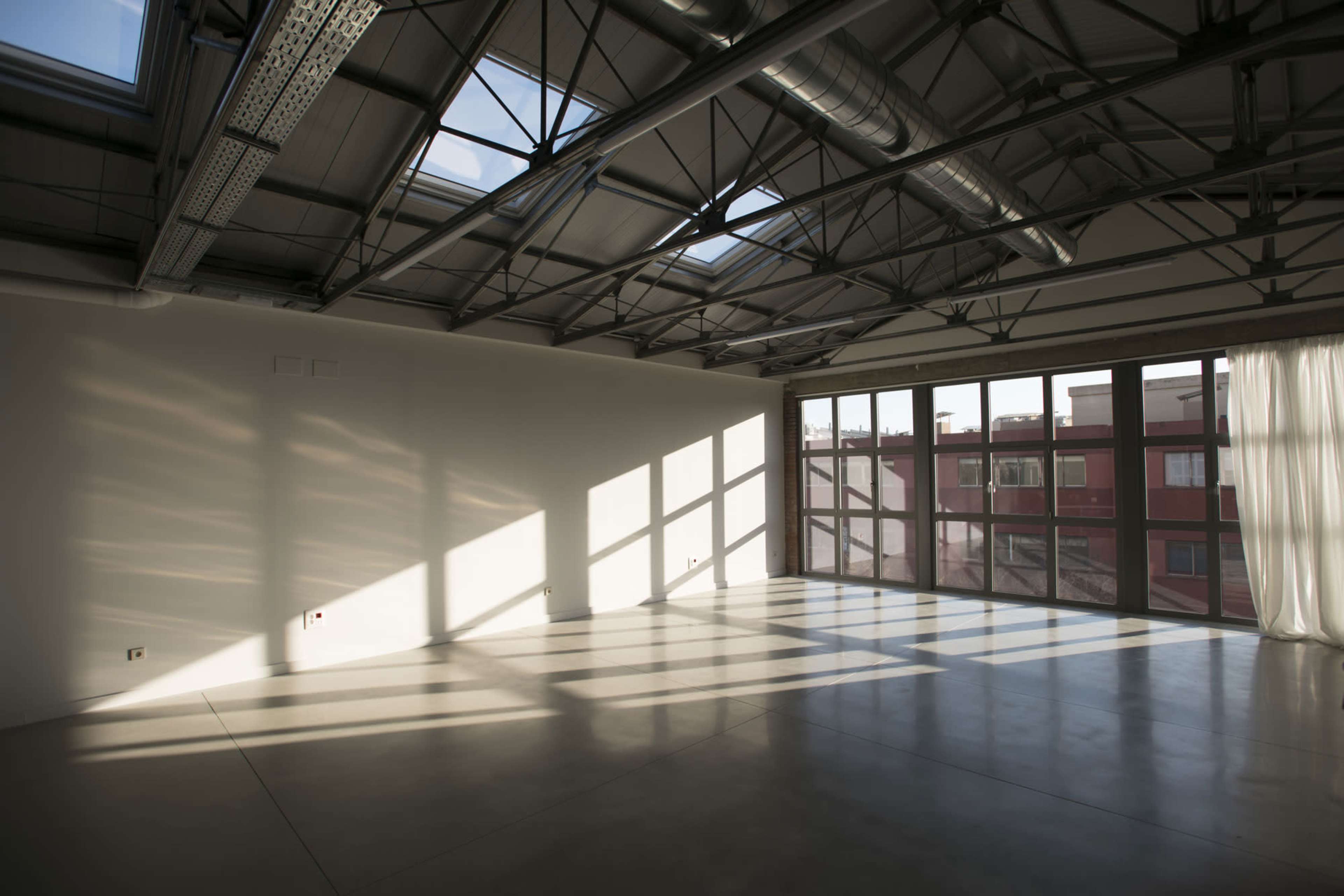 An empty room with large windows and skylights, casting shadows on the polished concrete floor.