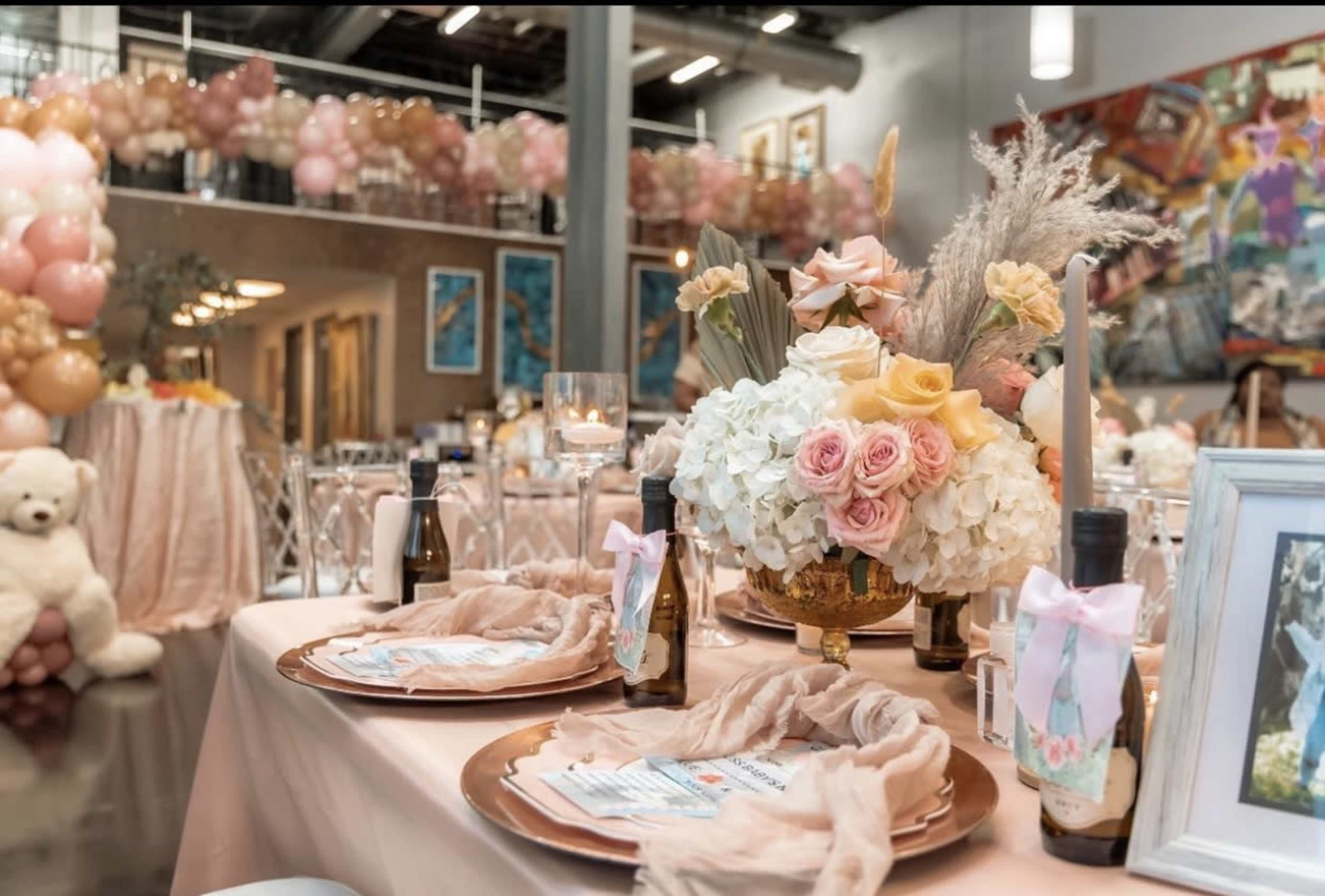 A elegantly set table for an event, featuring floral centerpieces, decorative plates, and bottles alongside a backdrop of balloon decorations.