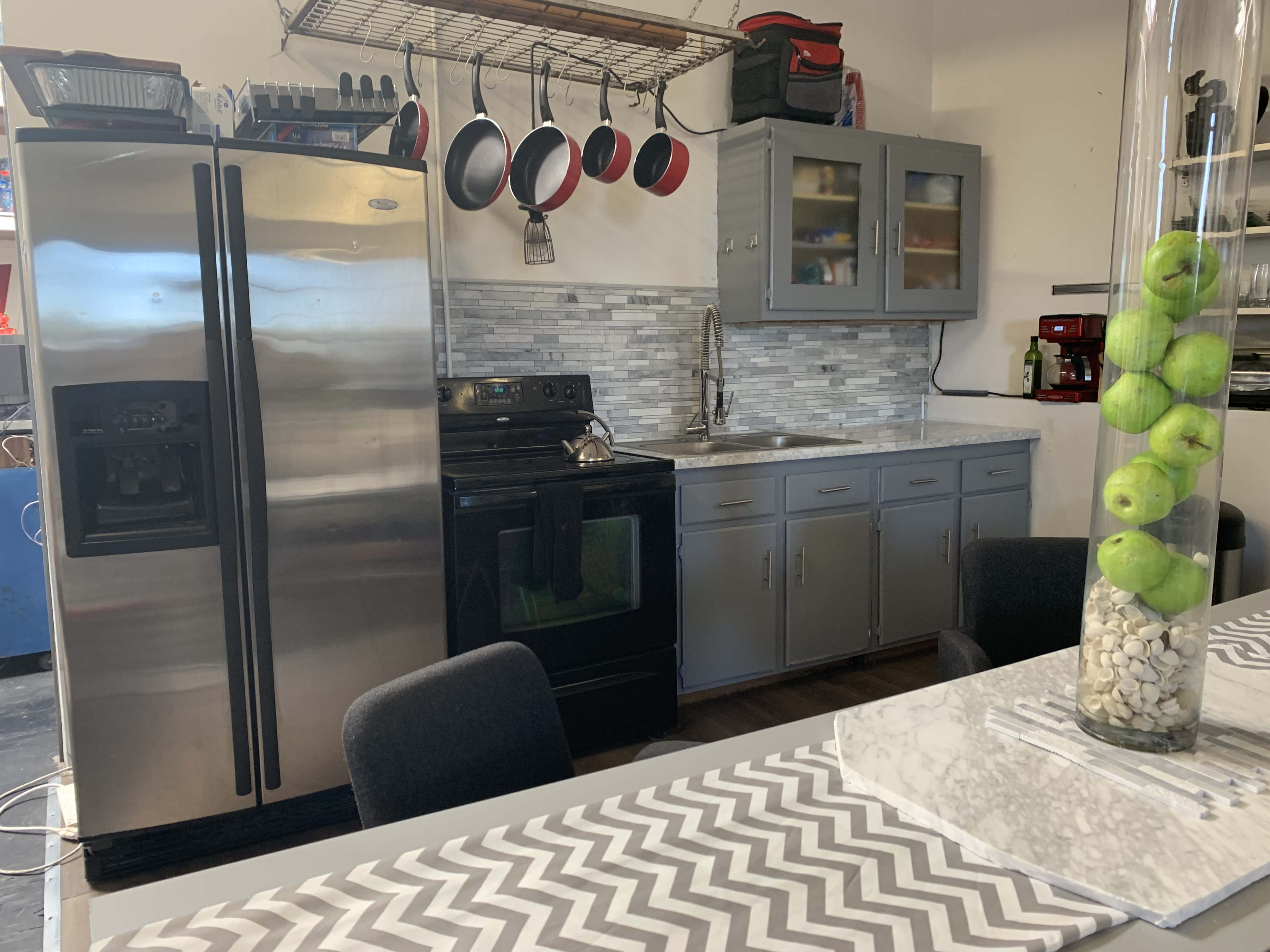 The image shows a modern kitchen with stainless steel appliances, gray cabinets, and a dining table with a patterned table runner.