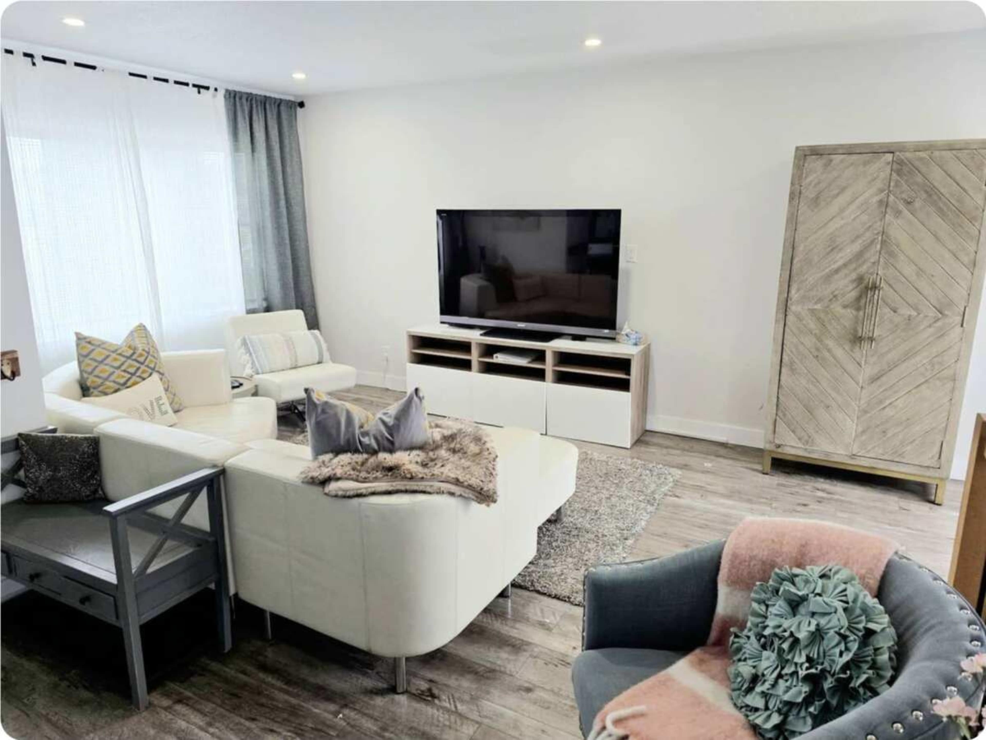 The image shows a modern living room with a white sectional sofa, a television on a console, and a cabinet in the corner.