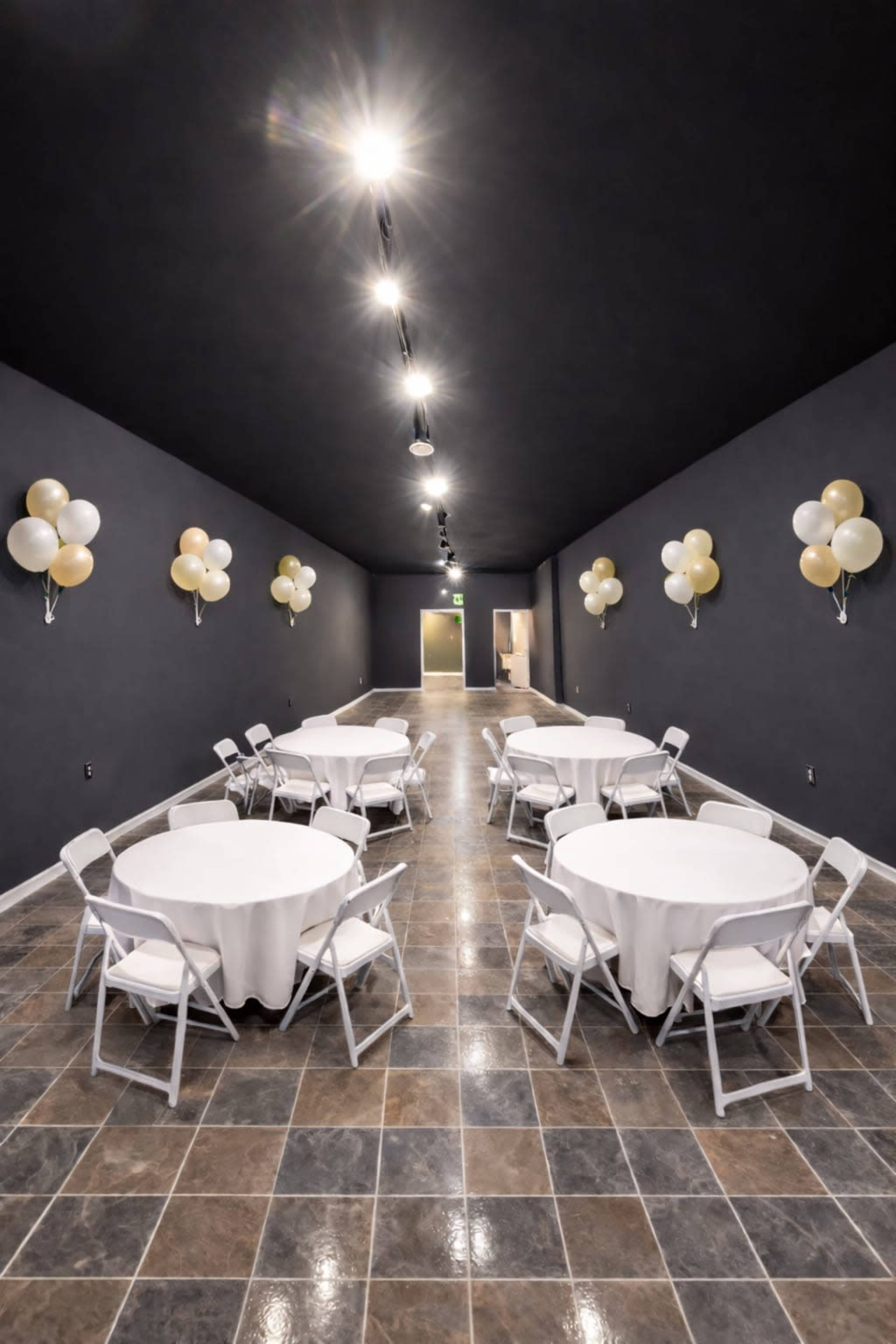 A long hallway features several round tables with white tablecloths and folding chairs, adorned by balloons on the walls.