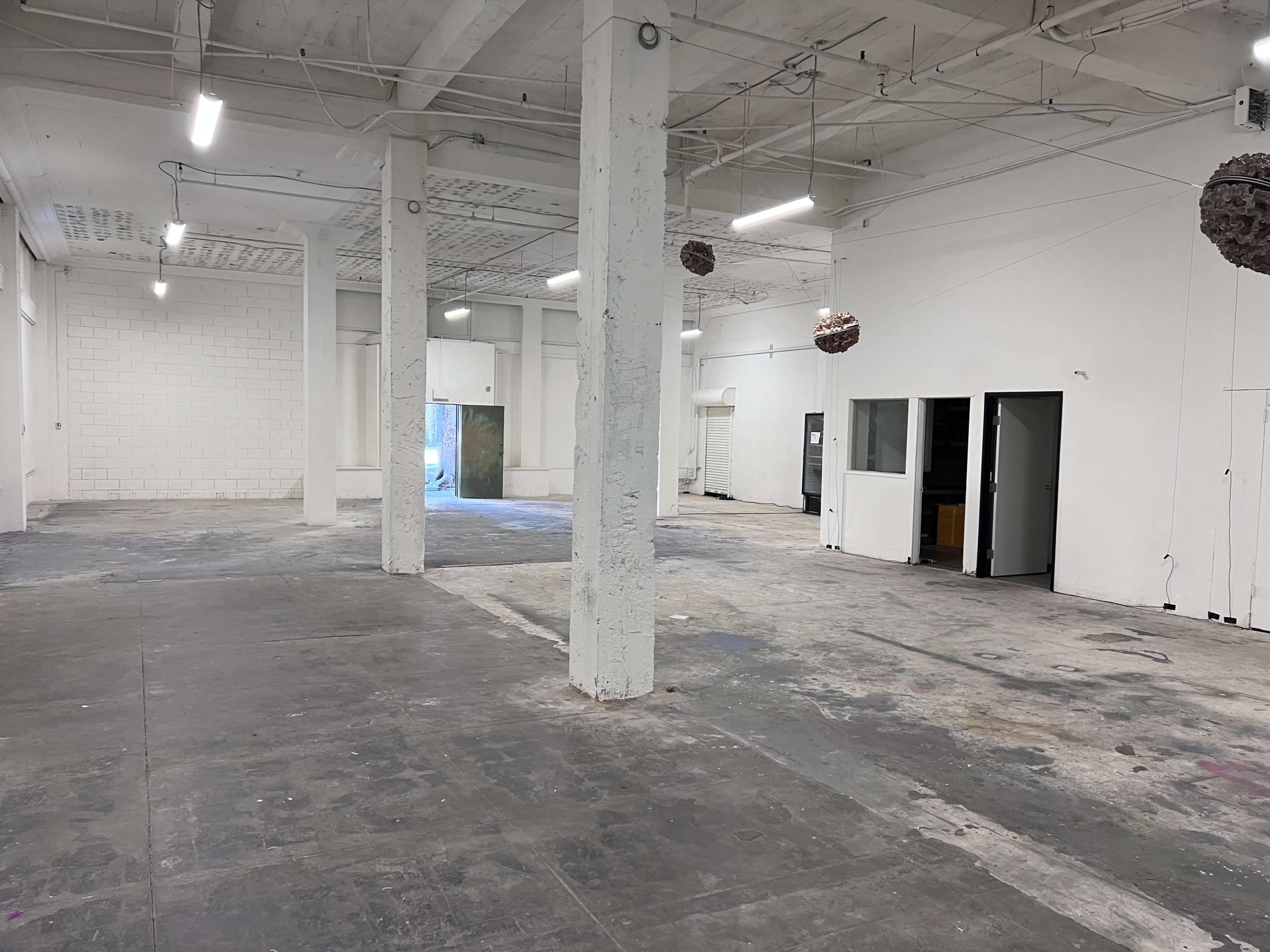 A spacious, empty interior of a building with concrete floors, white walls, and several columns.