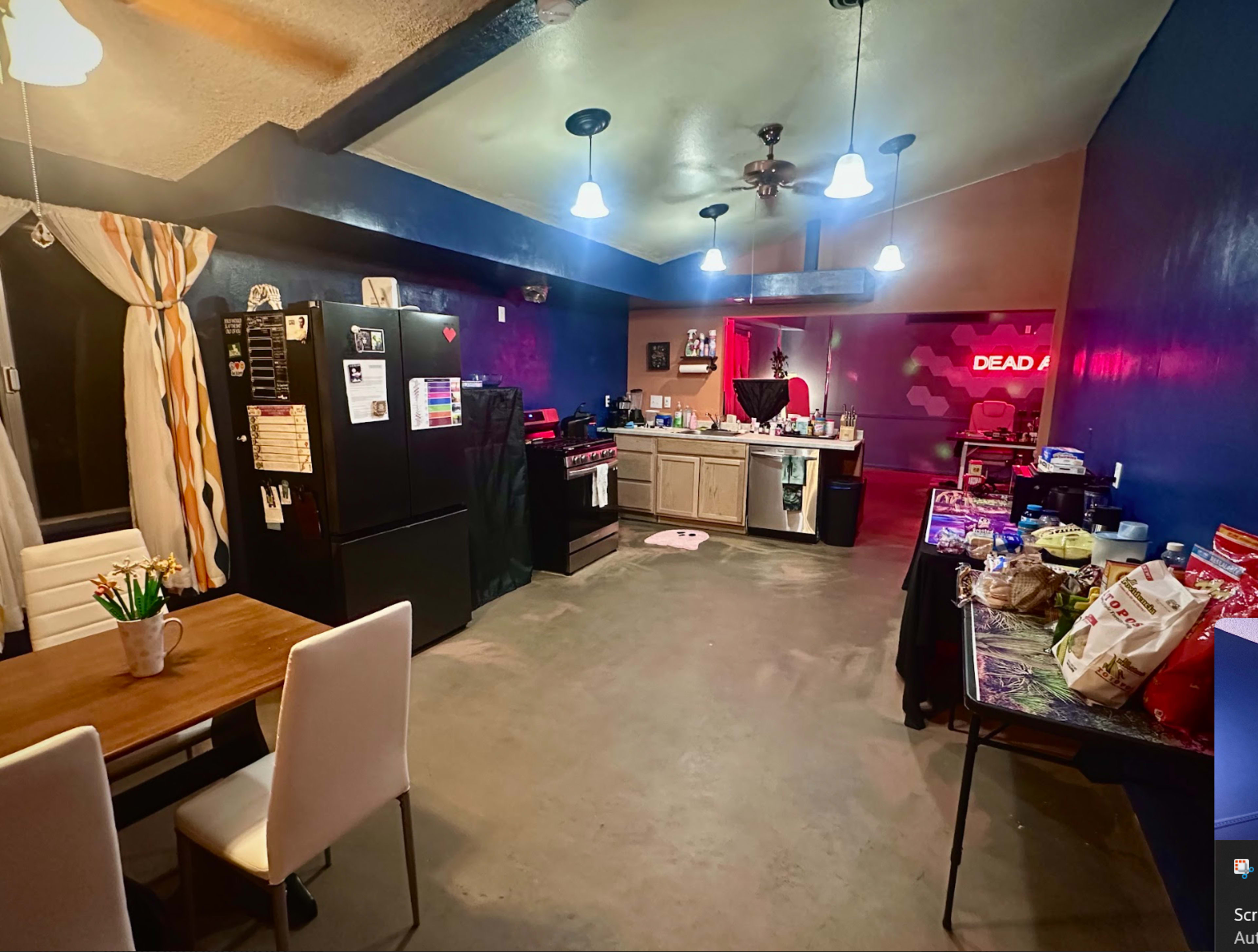 A spacious kitchen and dining area features a black refrigerator, a wooden table with white chairs, and various food items spread across counters.