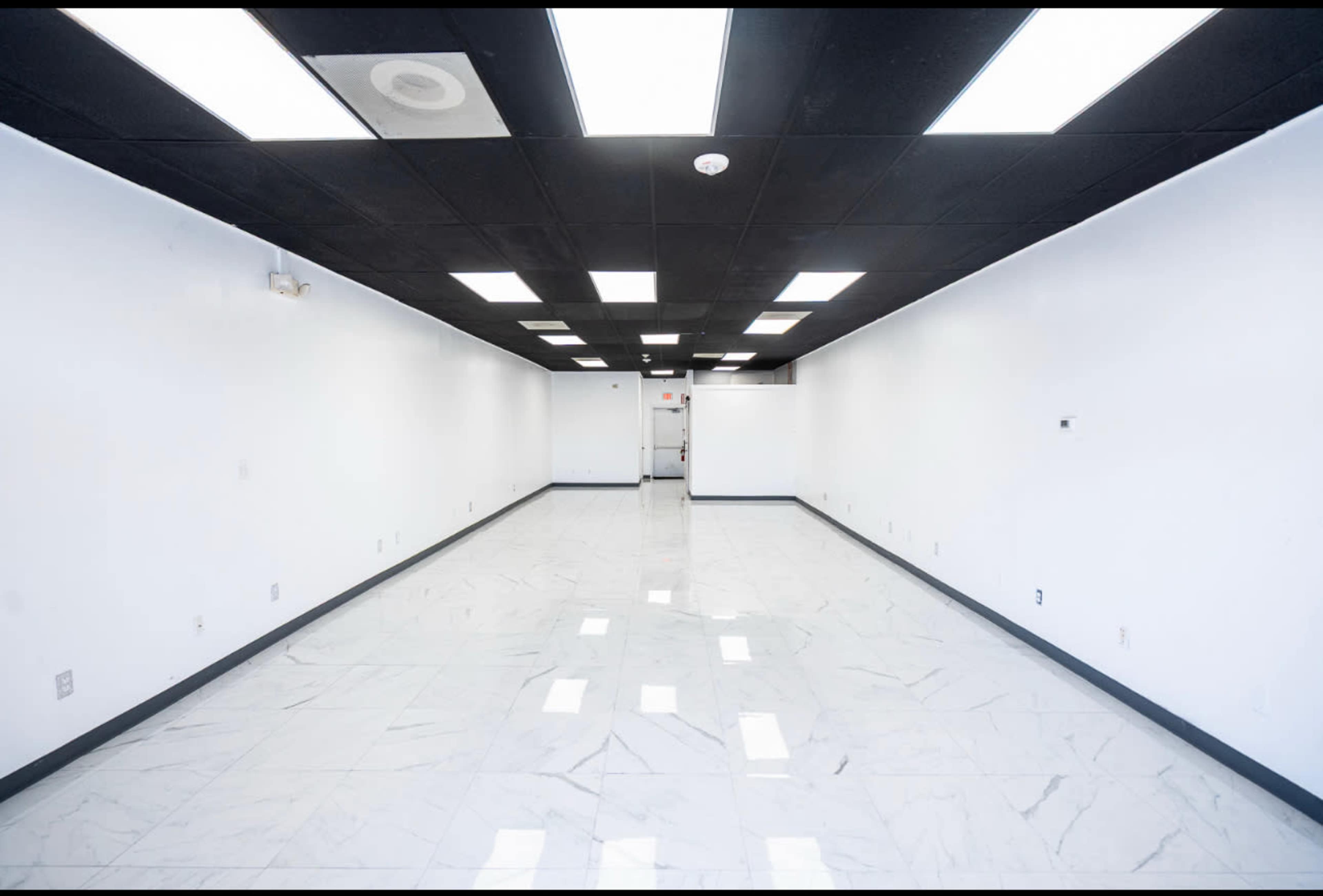 The image shows a large, empty room with white walls, a checkered black and white ceiling, and glossy marble flooring.