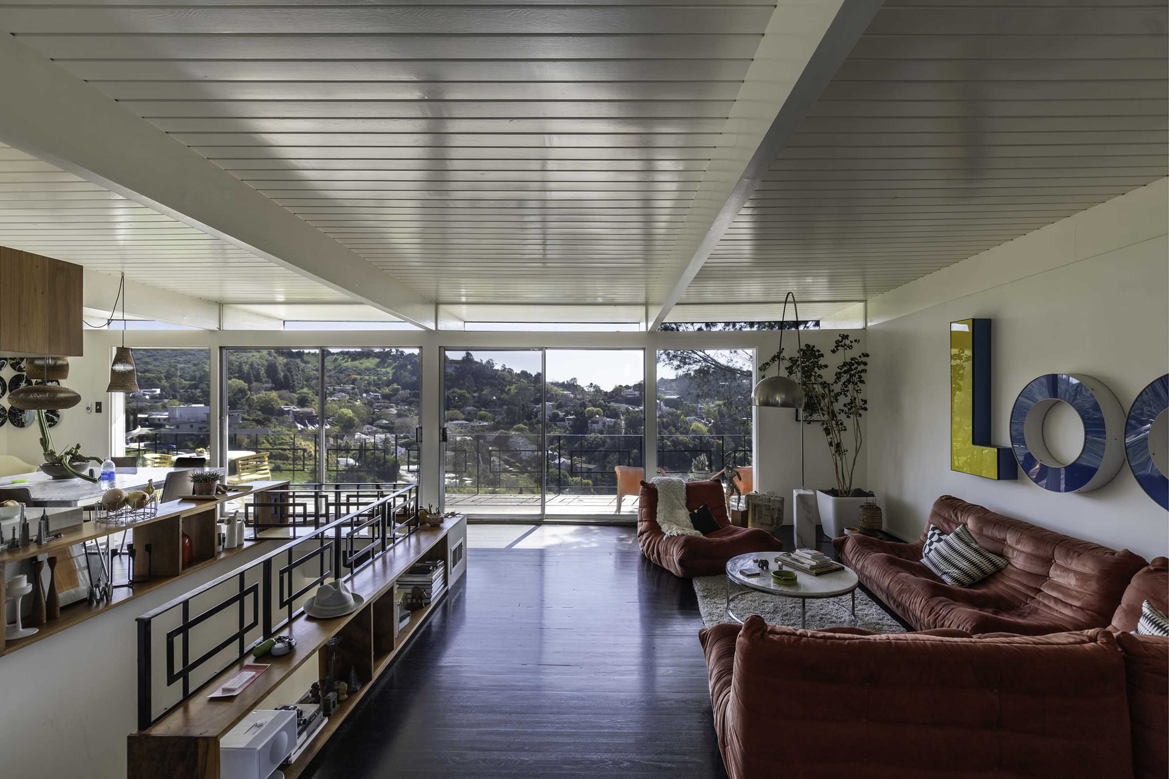 This interior features a spacious living area with large windows providing a view of the outdoors, surrounded by modern furnishings and decorative elements.